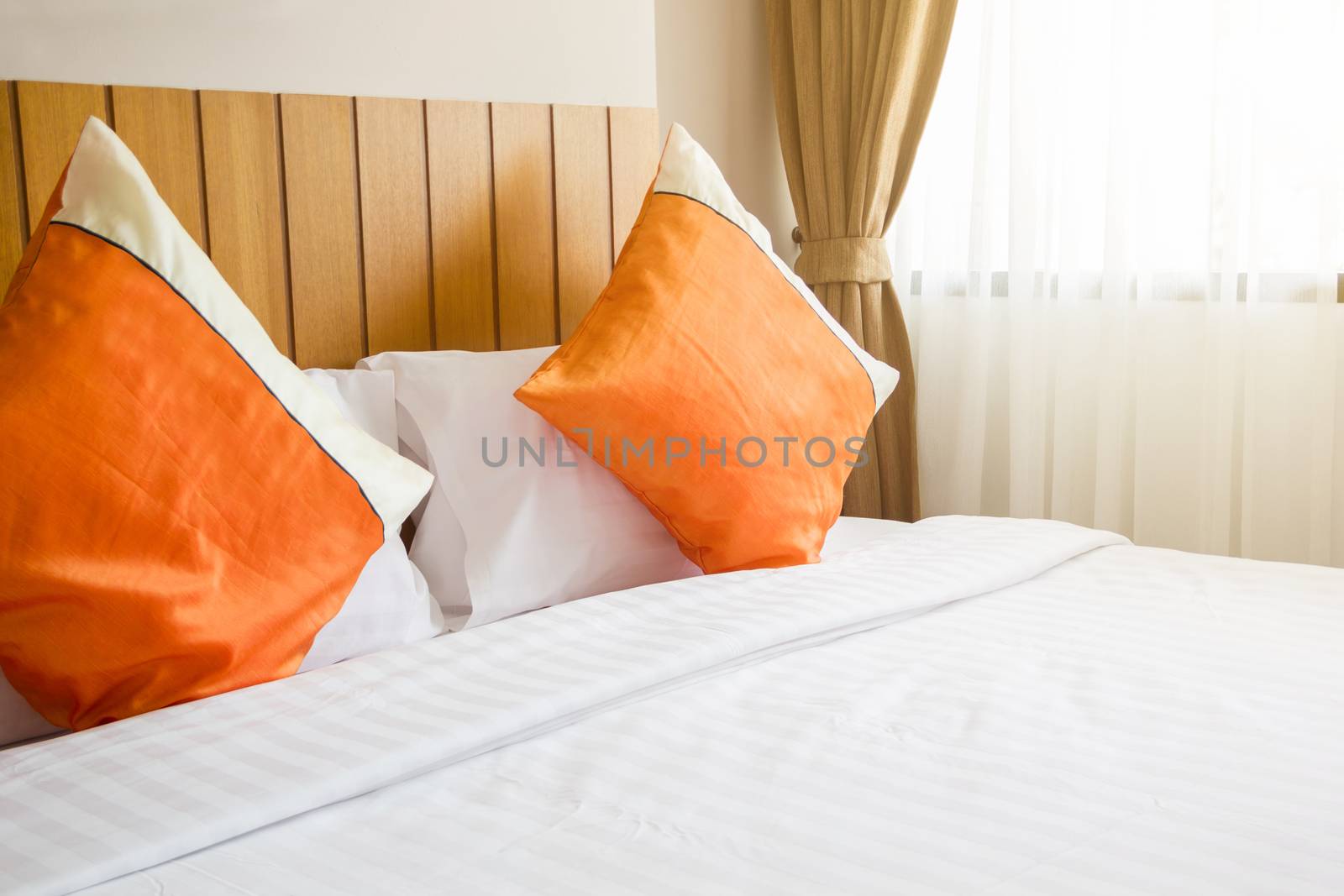 orange pillow and white blanket on bed in bedroom with lighting upper right side