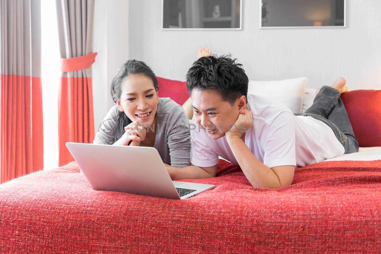 Young Asian Couples using laptop together in bedroom of contemporary house for modern lifestyle concept