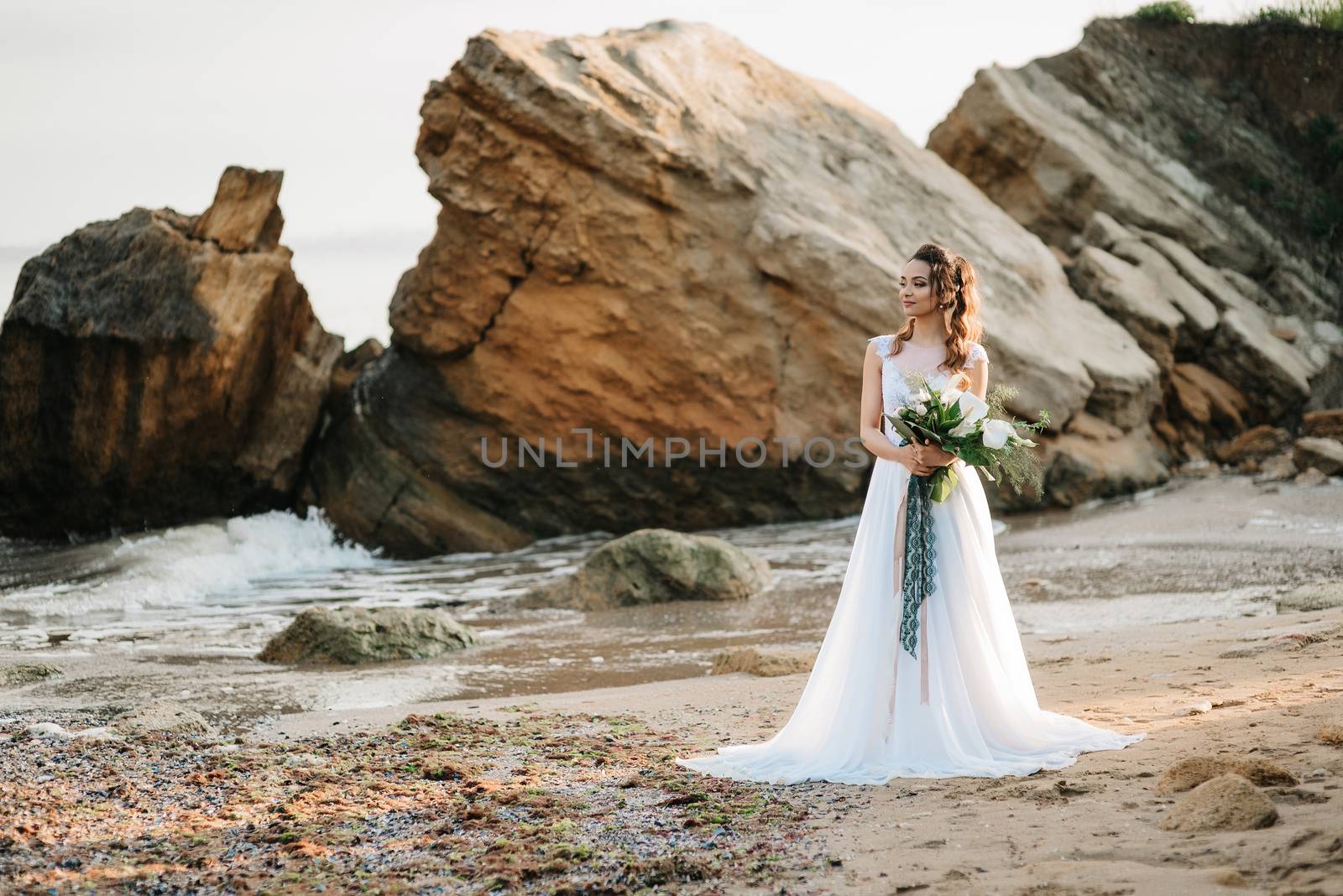 bride with a wedding bouquet on the shore of the black sea in the sunset light