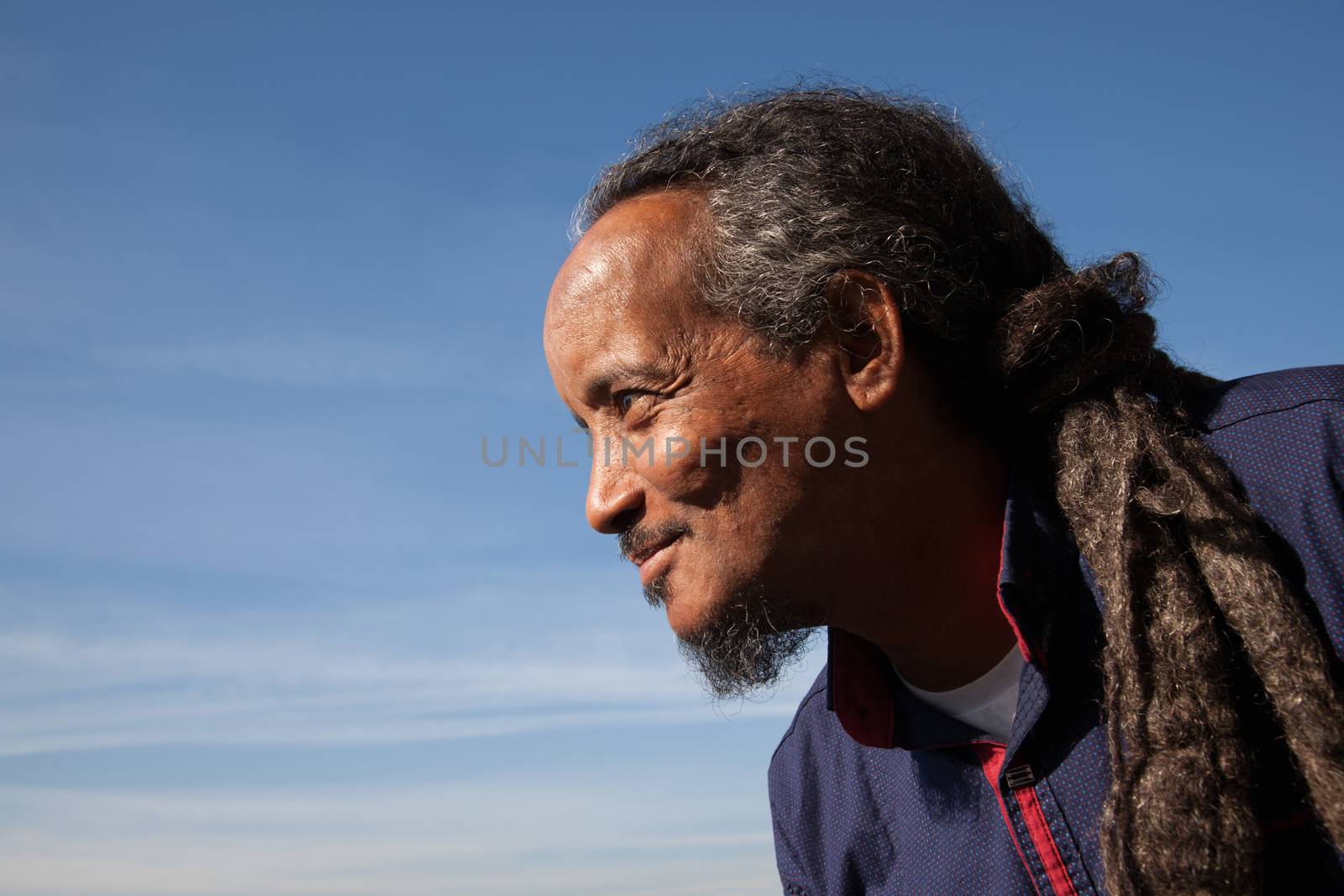 A portrait of a black rastafarian man over a blue sky with some clouds.