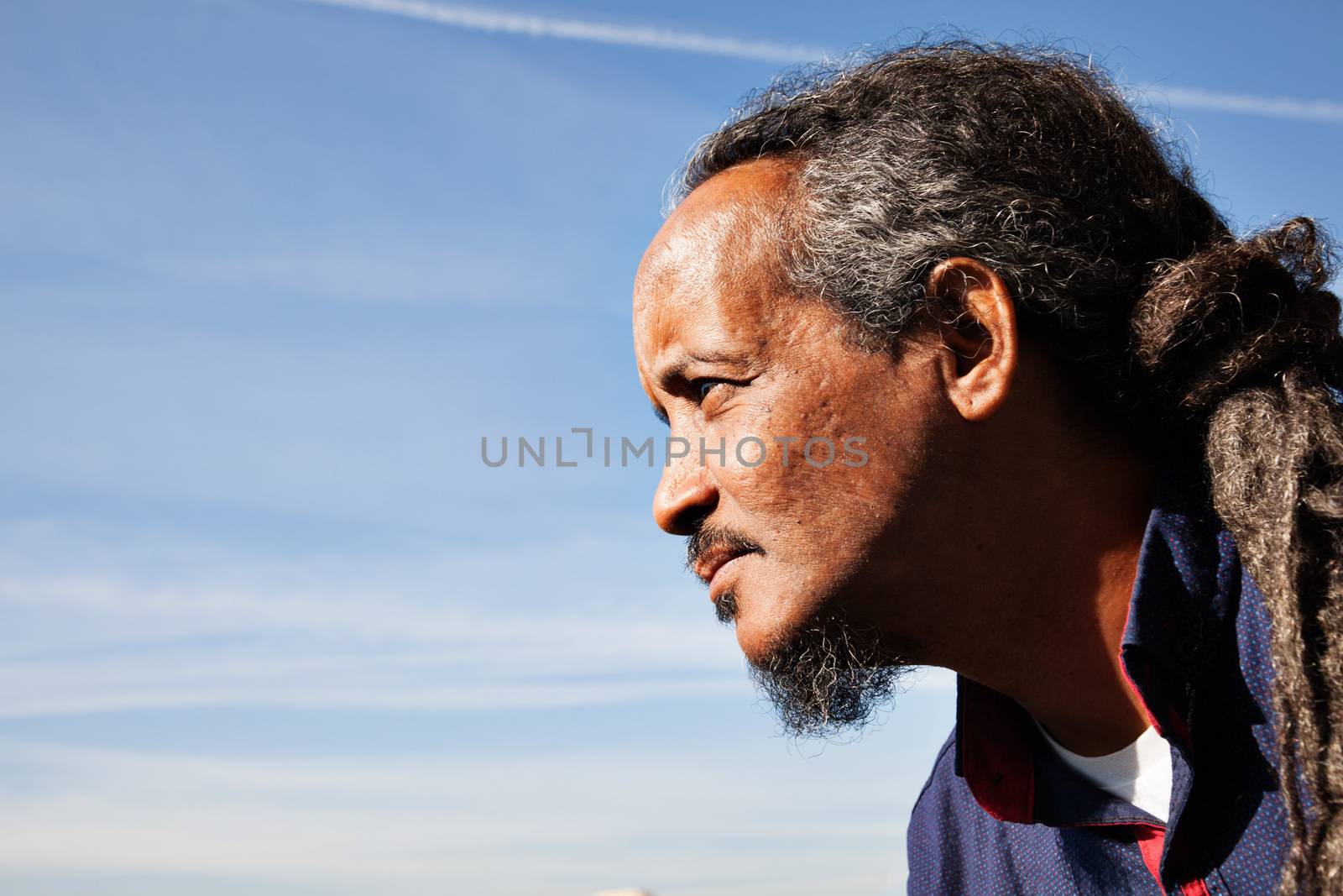 A portrait of a black rastafarian man over a blue sky with some clouds.