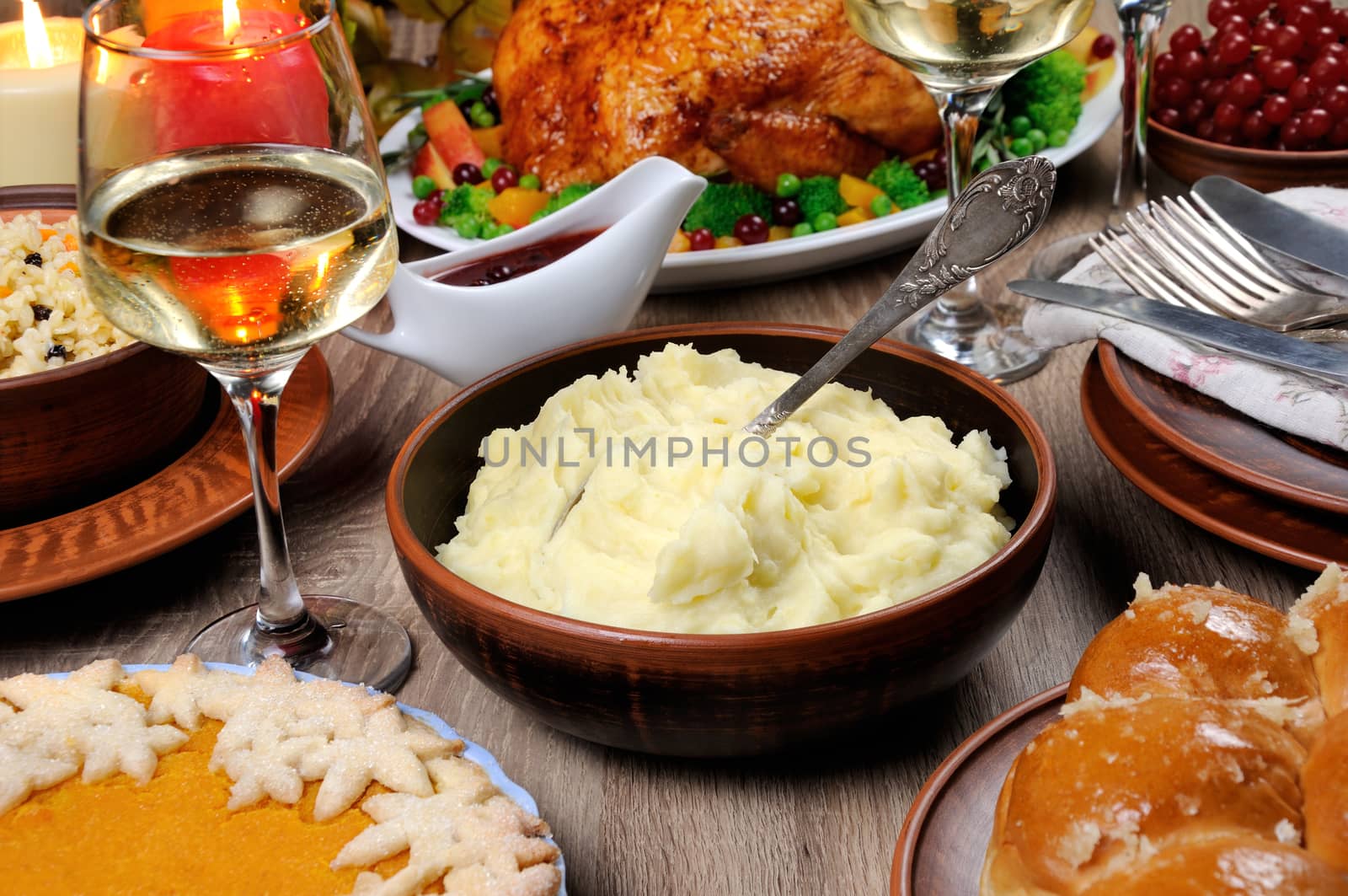 A bowl of mashed potatoes on a table among the pumpkin pie, baked turkey, cranberry-orange sauce,   a glass of white wine for Thanksgiving
