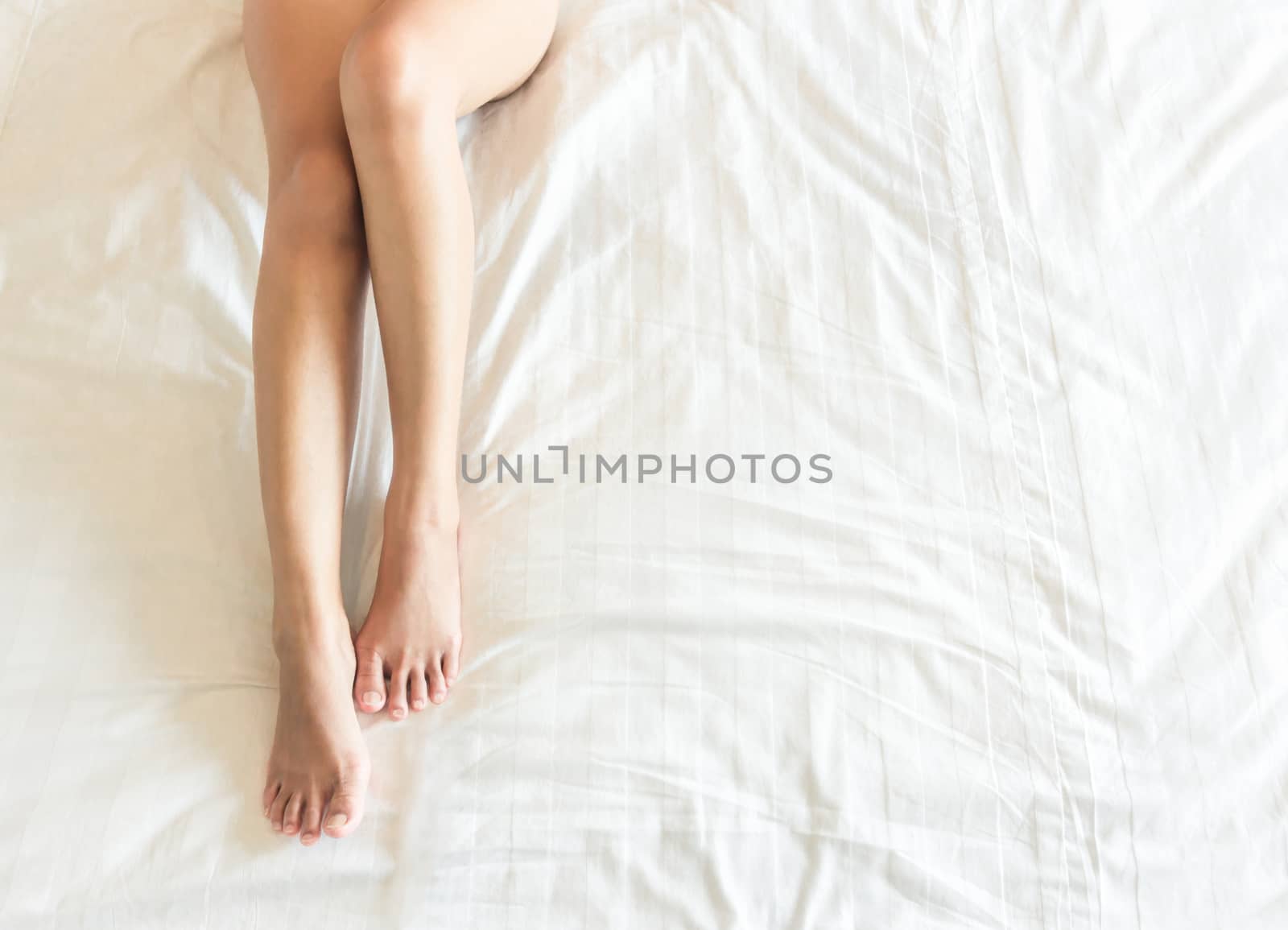 Closeup woman legs with sleeping on white bed, beauty and skin care concept, selective focus