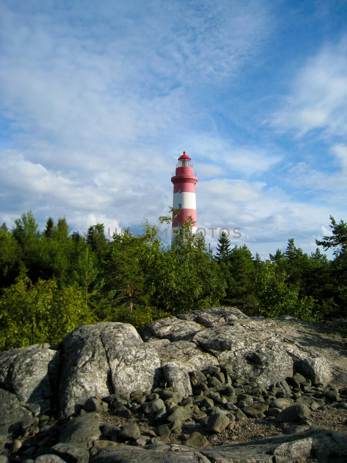 A lighthouse on the shore with some rocks in front