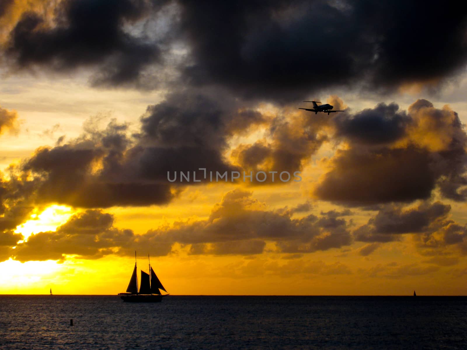 A sailboat sailing in the sunset while an airplane prepares for landing