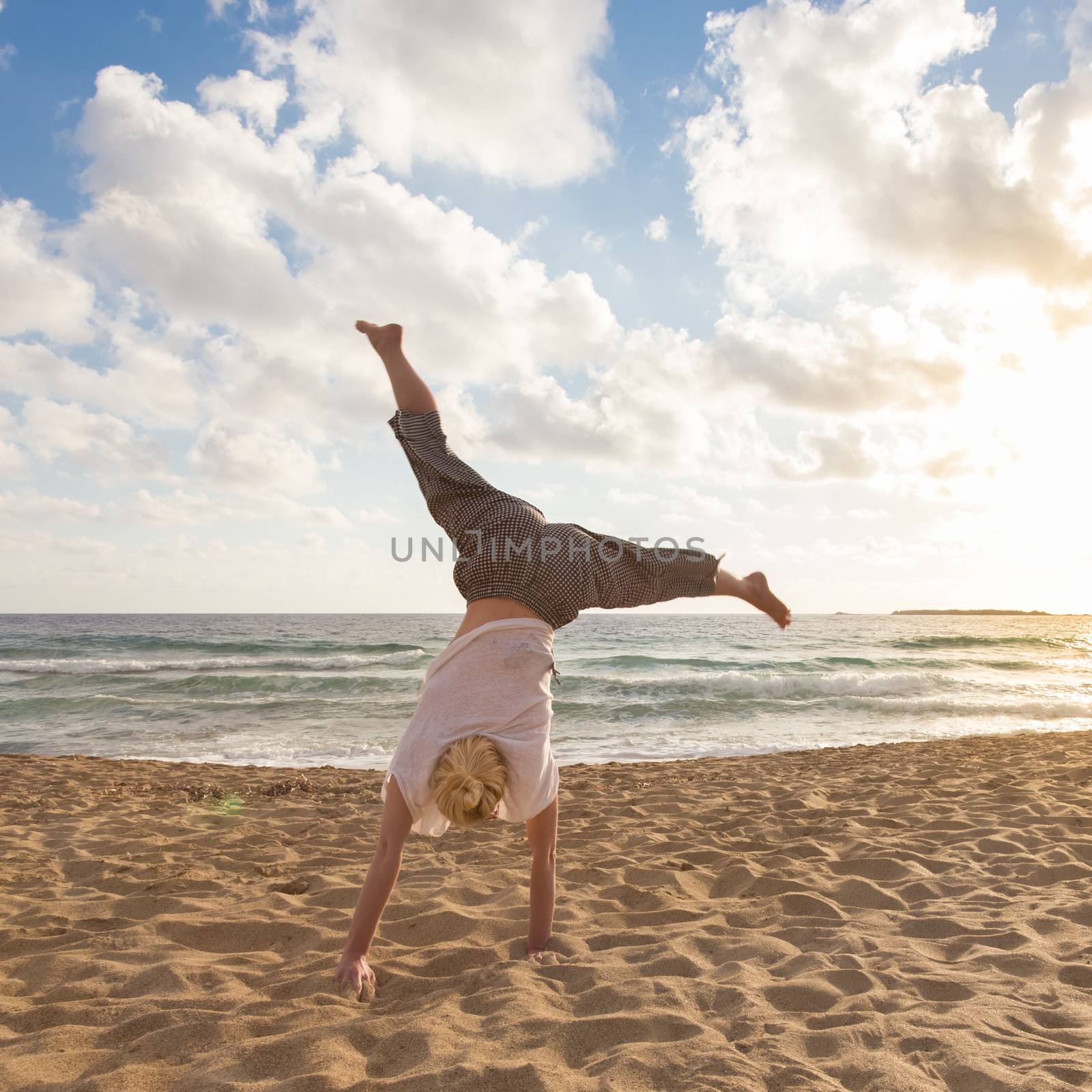 Relaxed woman enjoying sun, freedom and life turning cartwheel on beautiful beach in sunset. Young lady feeling free, relaxed and happy. Vacations, freedom, happiness, enjoyment and well being.