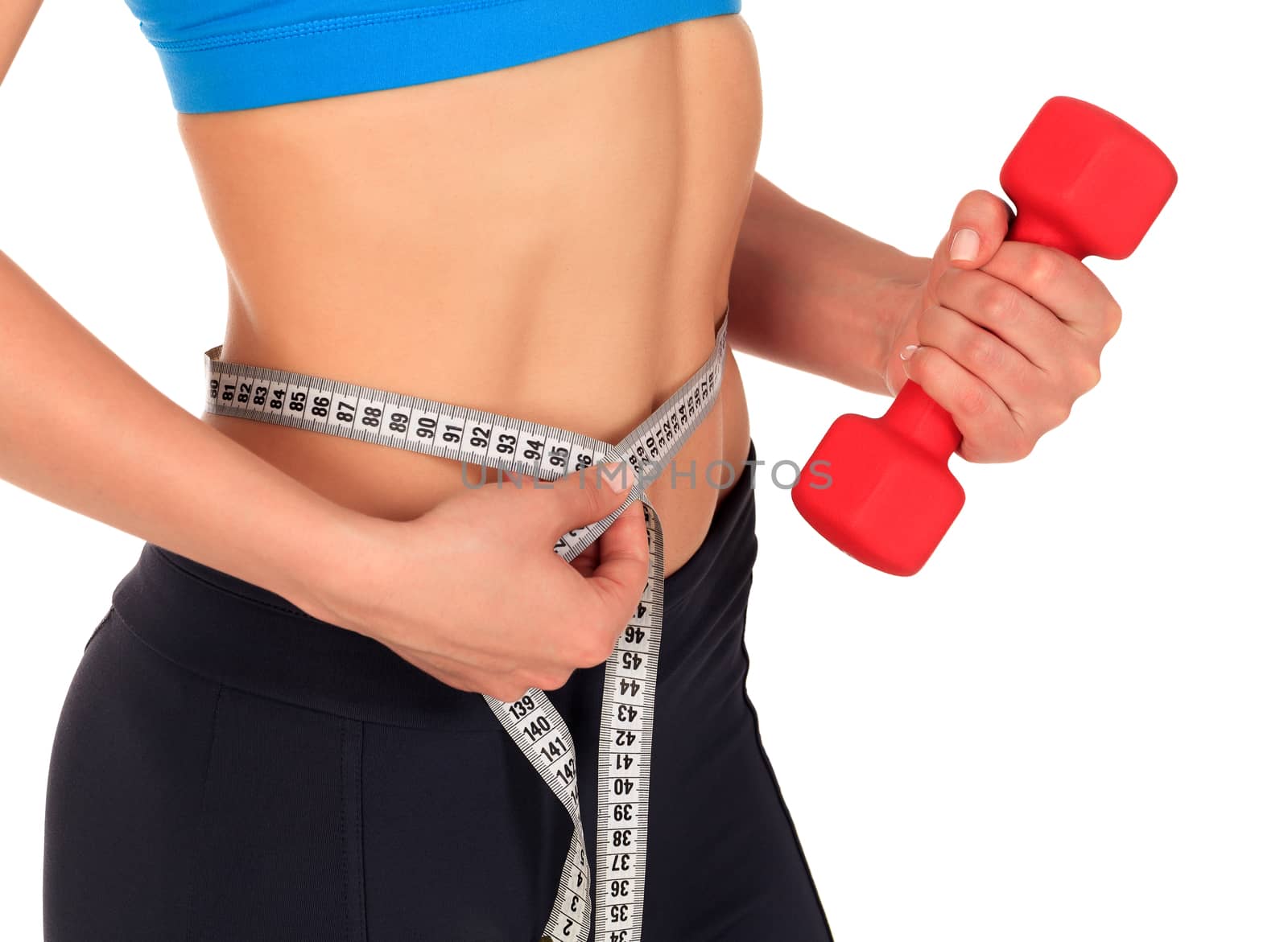 Closeup shot of slim young woman holding red dumbbell and measuring her thin waist with a tape measure, isolated on white background