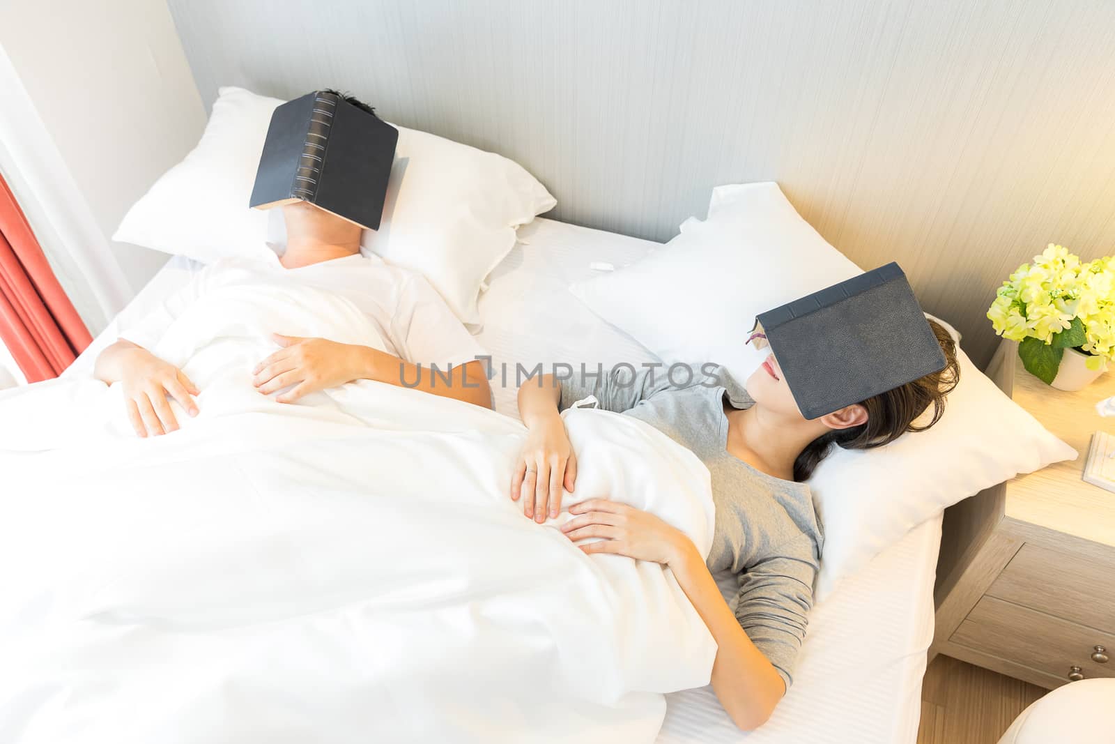 Young Asian Couple laid in a bed reading a book in bedroom of contemporary house for modern lifestyle concept