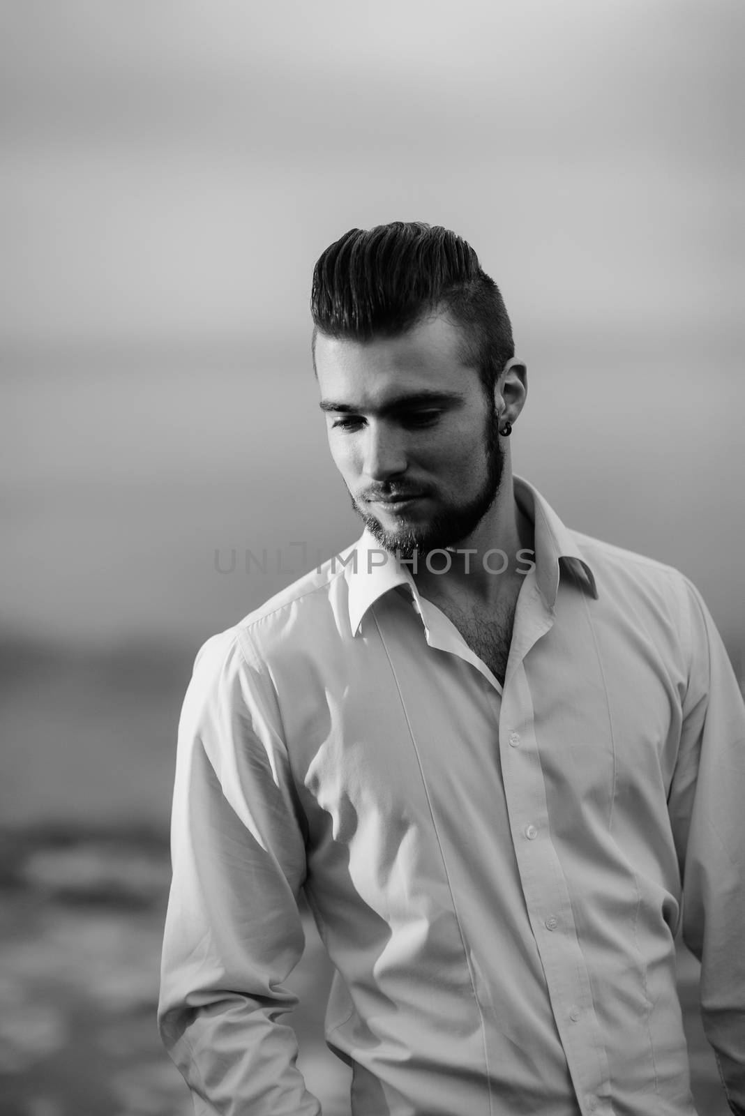 guy with a beard against the sea in the evening in a white shirt, portrait