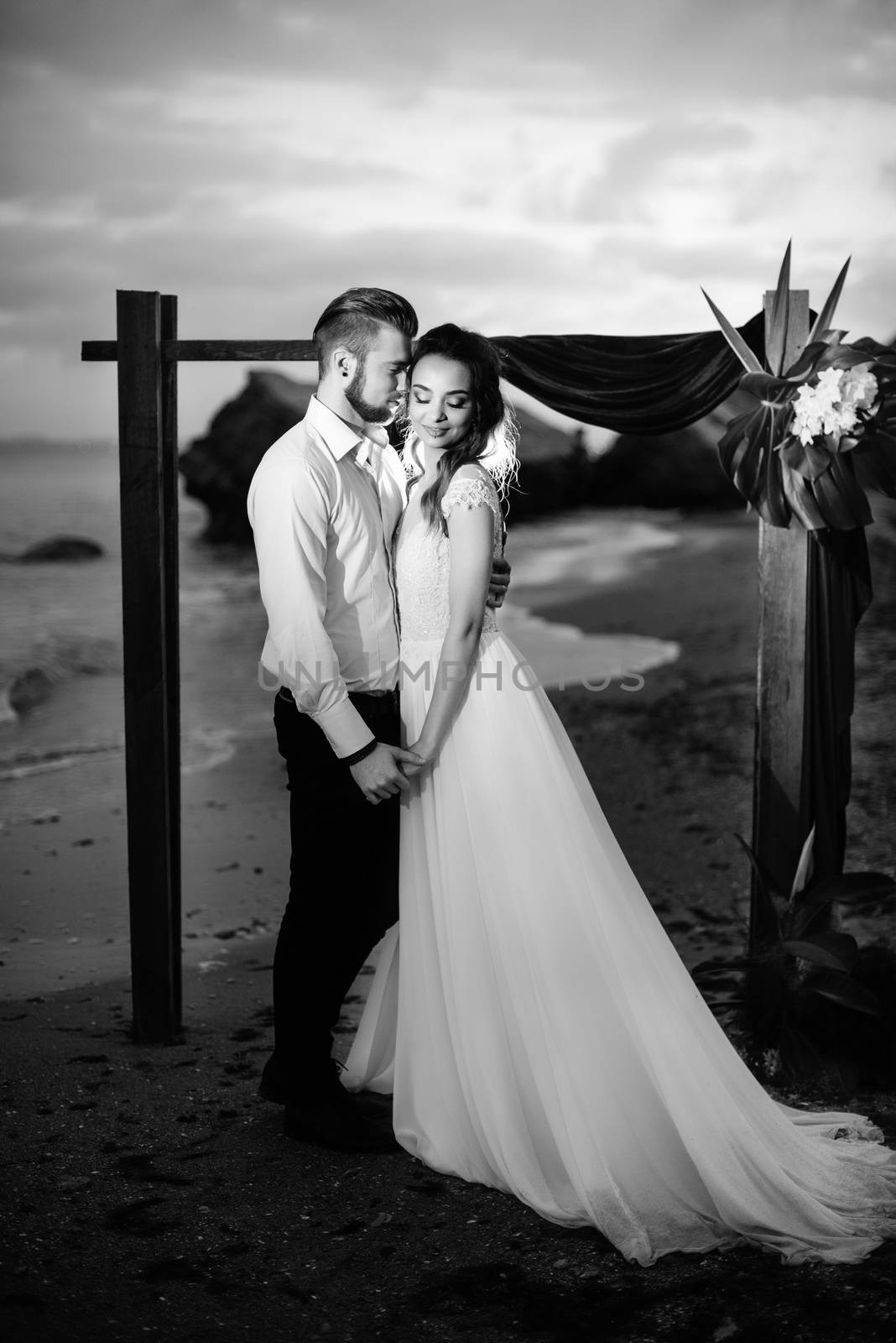 young couple groom and bride with a bouquet in the evening on the beach near the wedding arch