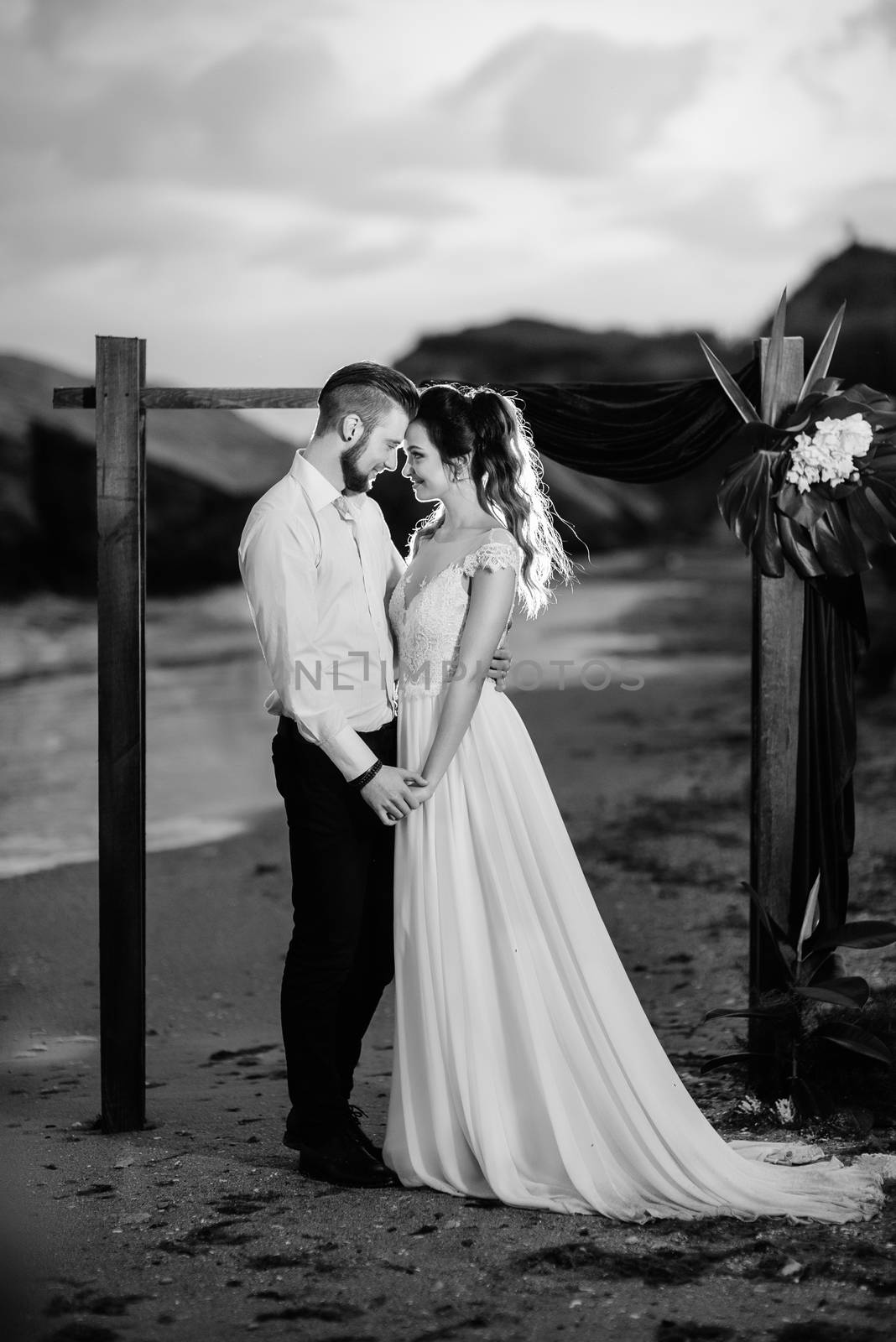 young couple groom and bride with a bouquet in the evening on the beach near the wedding arch