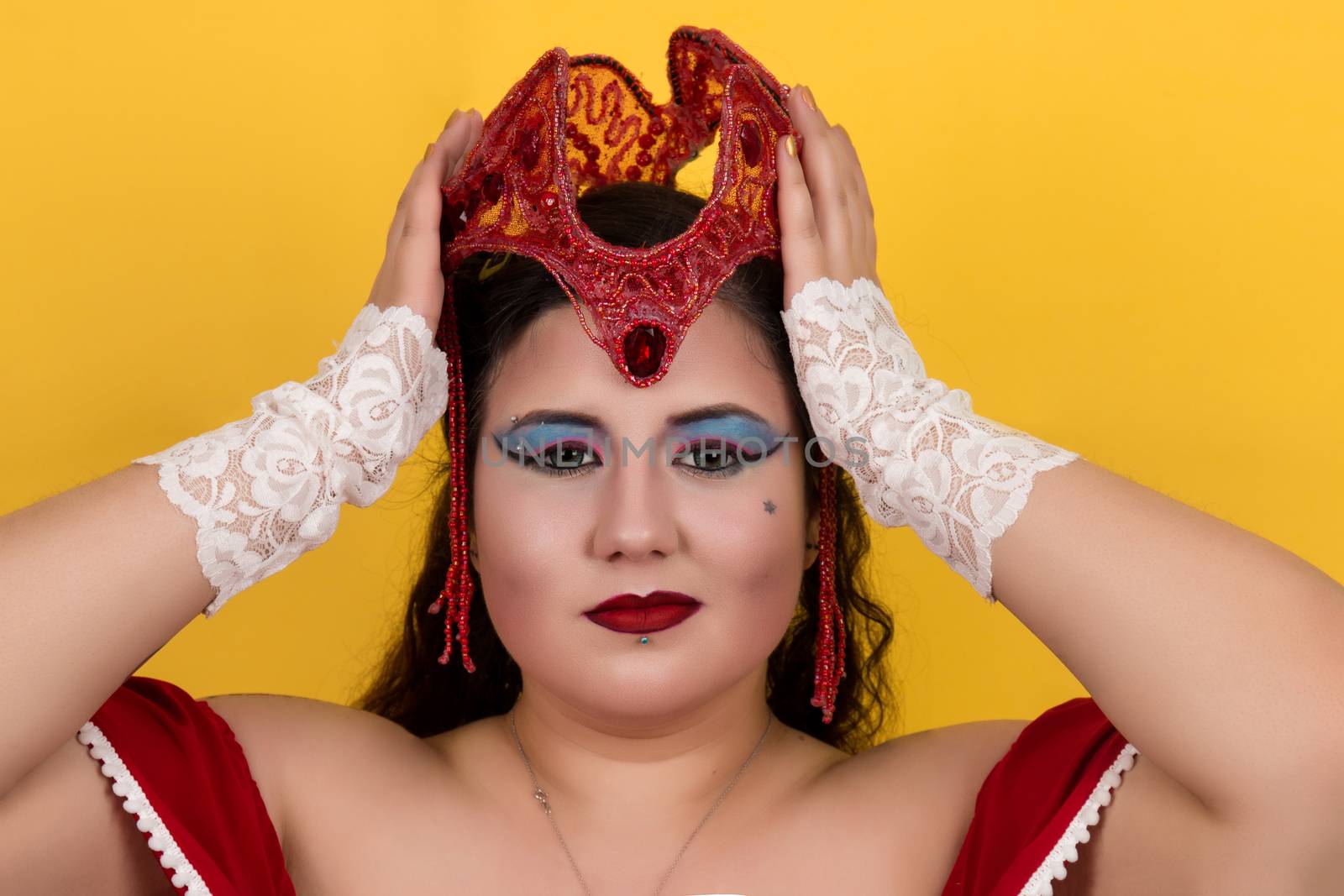 View of pinup vintage girl holding a red fantasy crown over a yellow background.