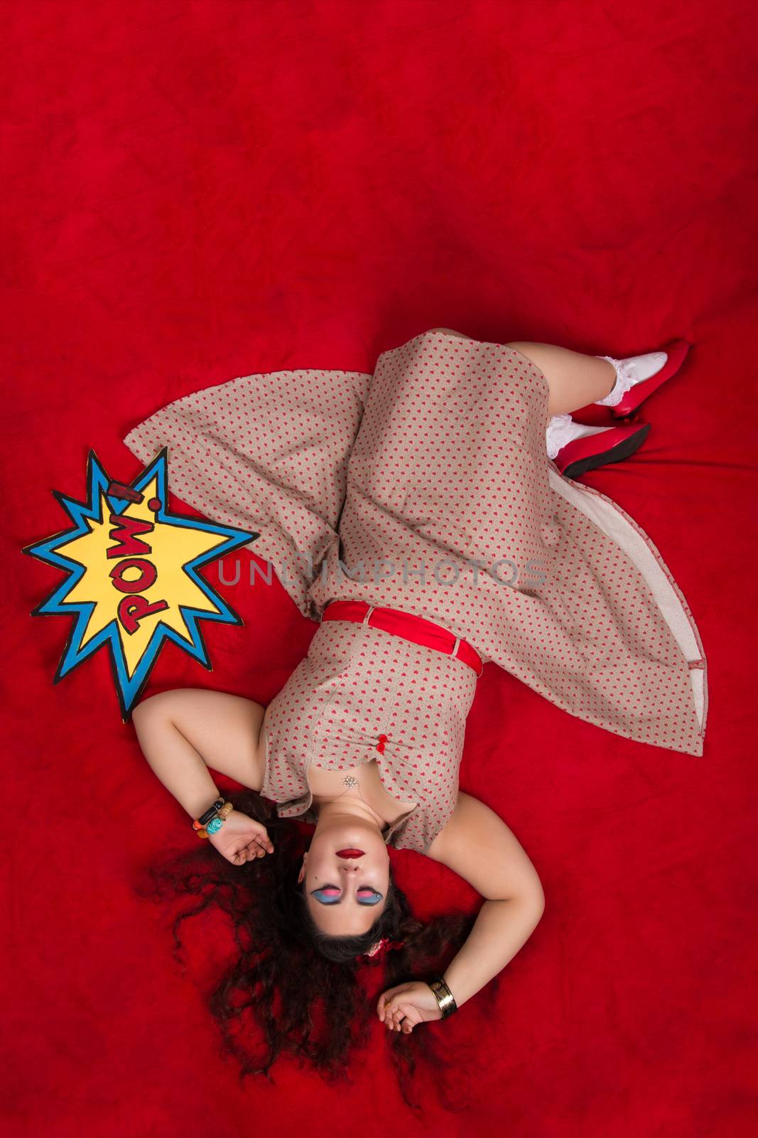 Pinup girl posing on red blacket bed in her bedroom.