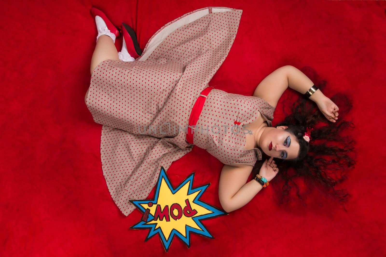 Pinup girl posing on red blacket bed in her bedroom.