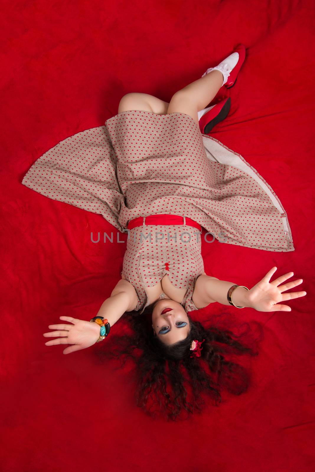 Pinup girl posing on red blacket bed in her bedroom.