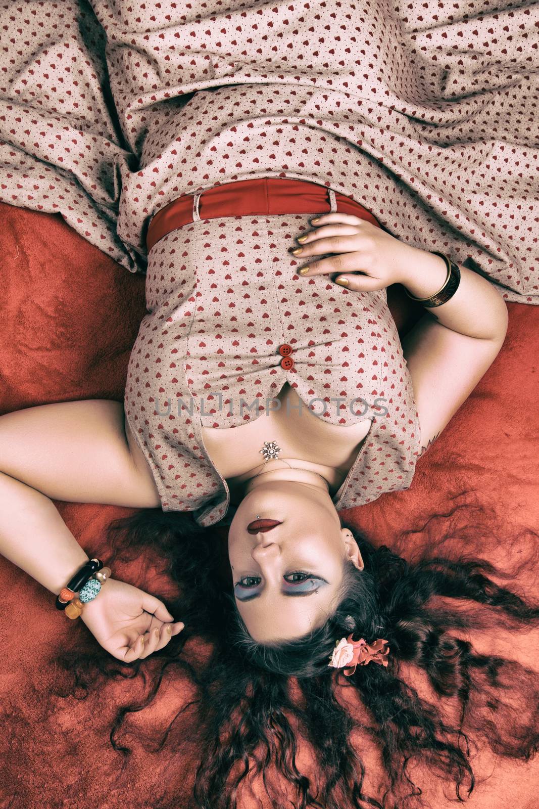 Pinup girl posing on red blacket bed in her bedroom.