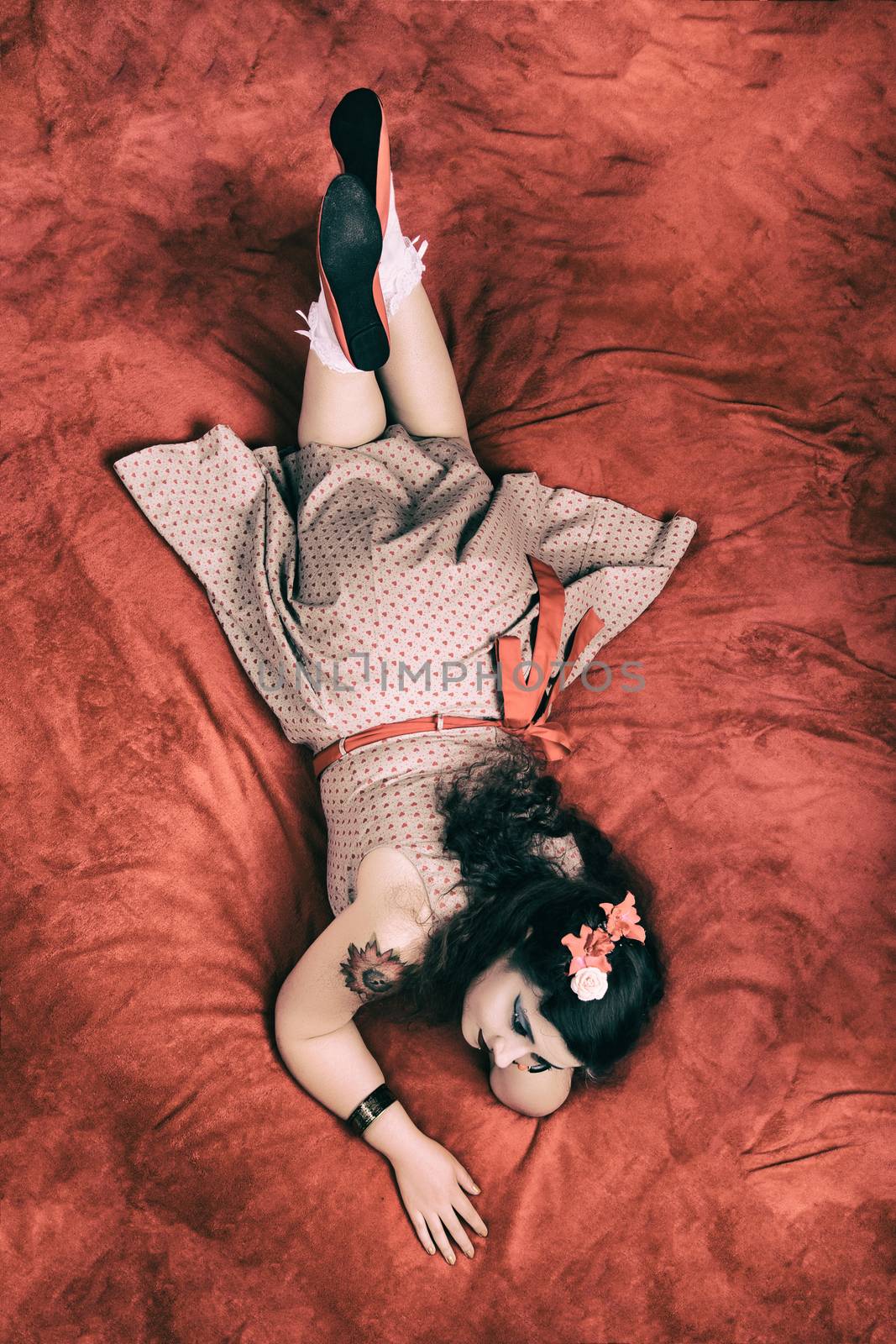 Pinup girl posing on red blacket bed in her bedroom.