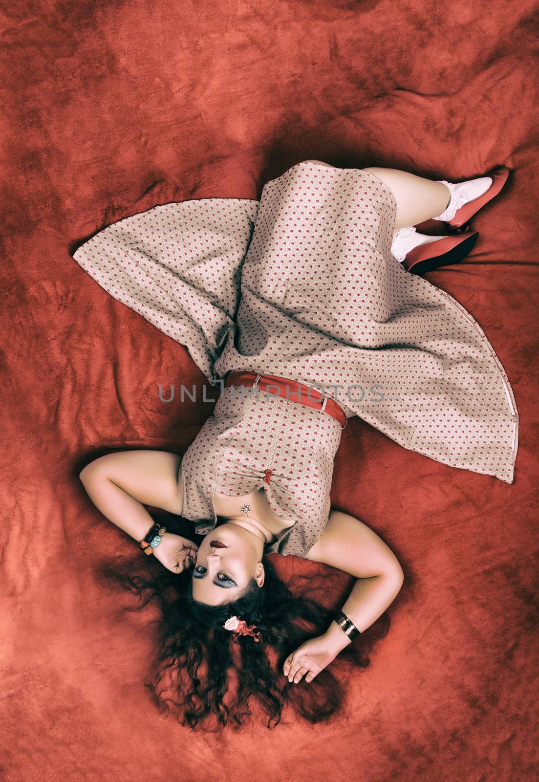 Pinup girl posing on red blacket bed in her bedroom.