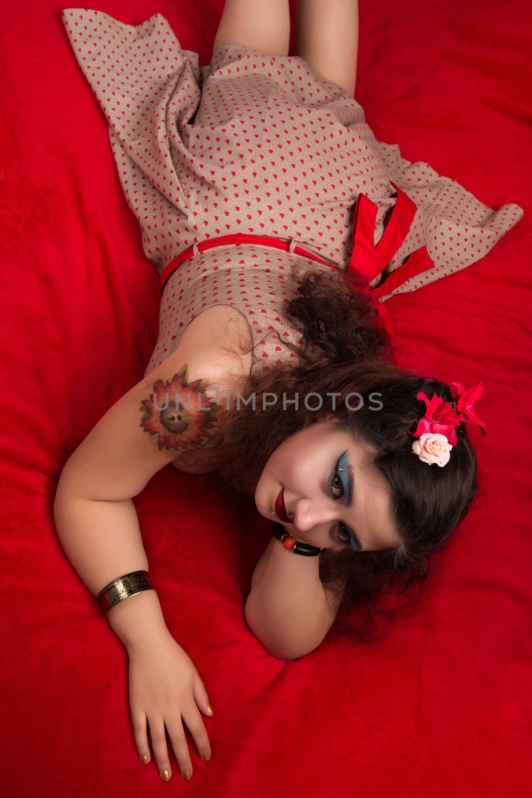 Pinup girl posing on red blacket bed in her bedroom.