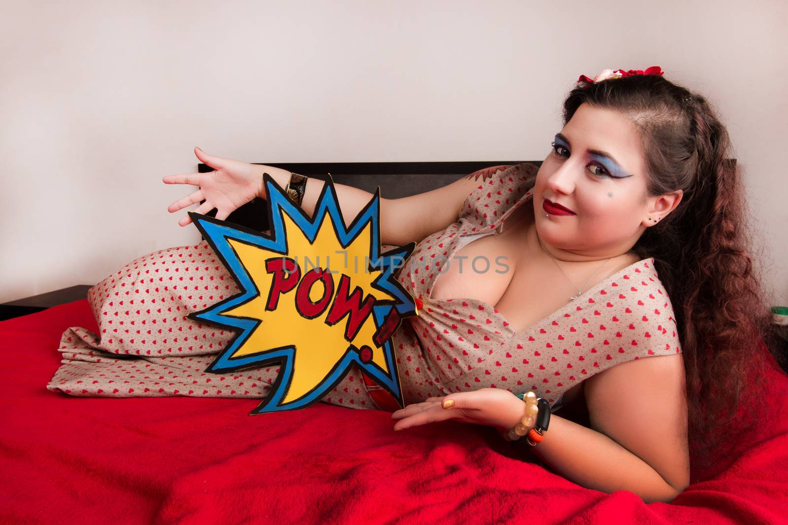 Pinup girl posing on red blacket bed in her bedroom.
