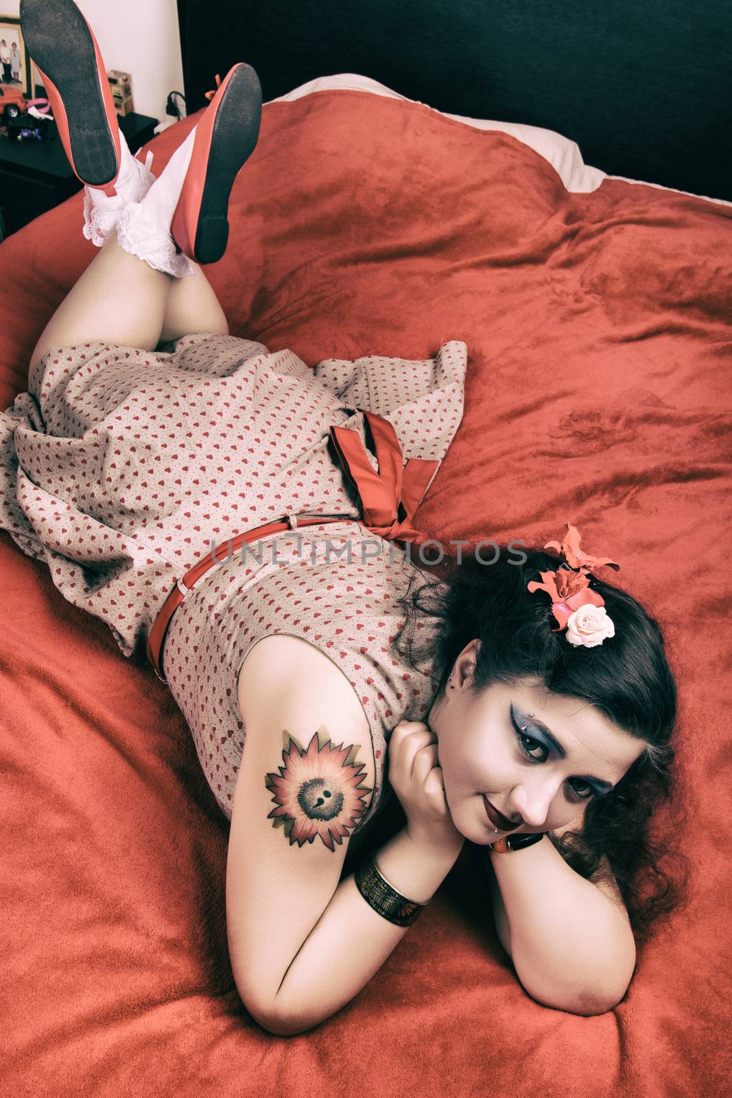 Pinup girl posing on red blacket bed in her bedroom.