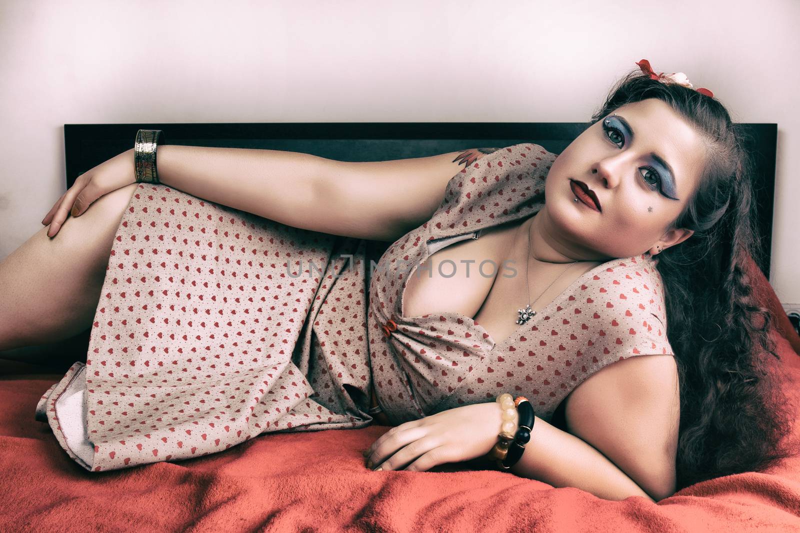 Pinup girl posing on red blacket bed in her bedroom.