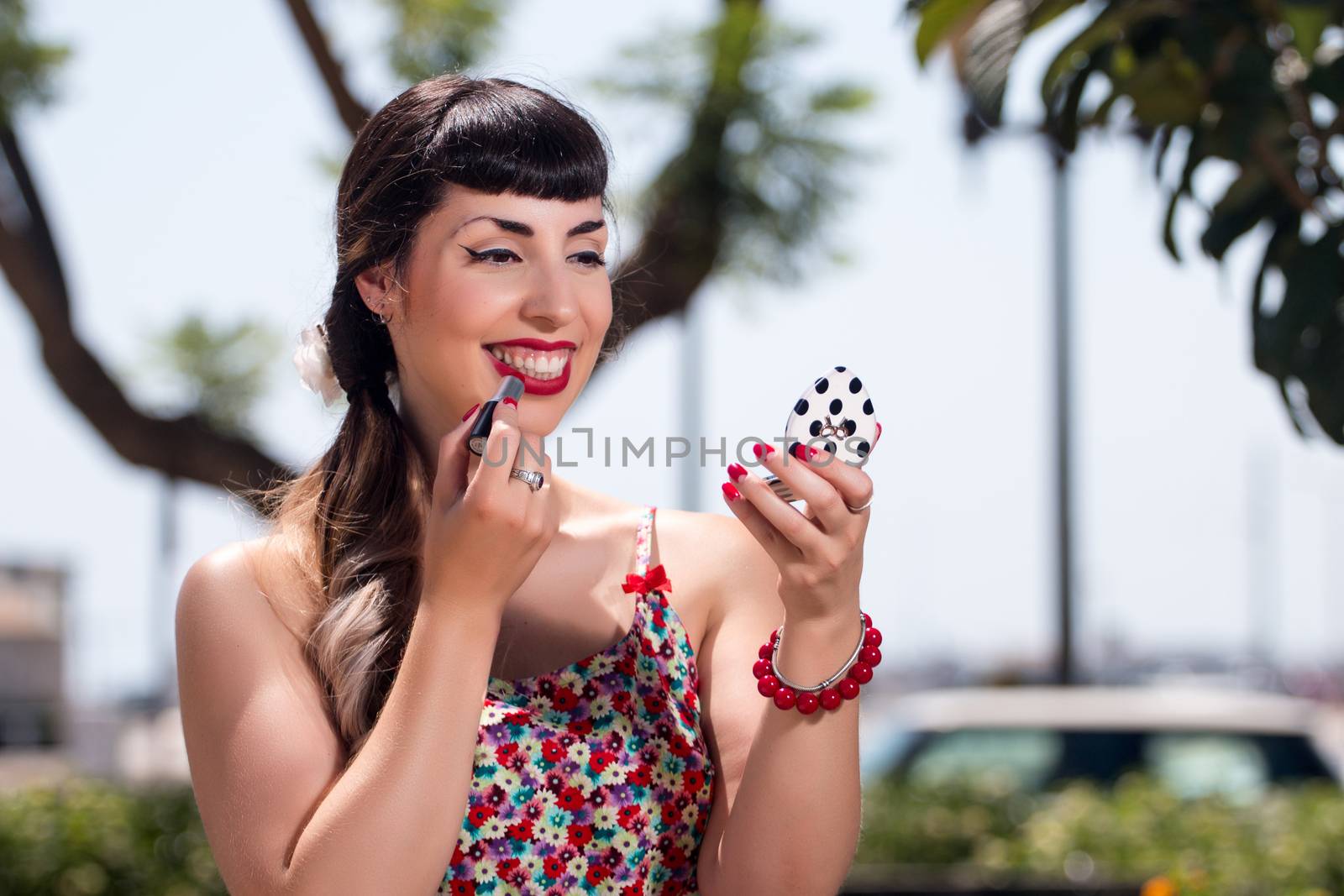 Pinup girl applying lipstick in a beautiful urban park.