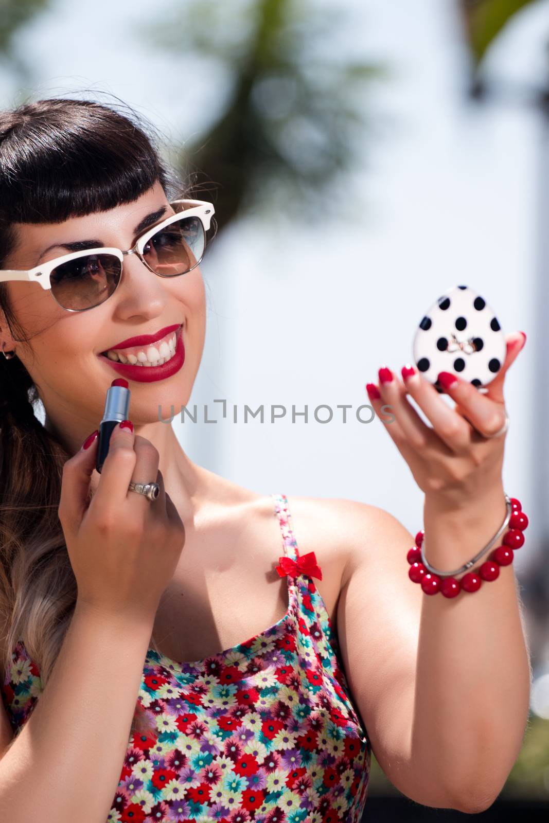 Pinup girl applying lipstick in a beautiful urban park.