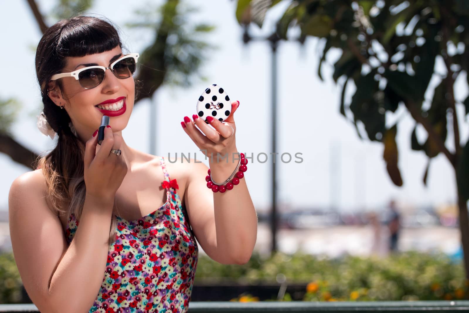 Pinup girl applying lipstick in a beautiful urban park.