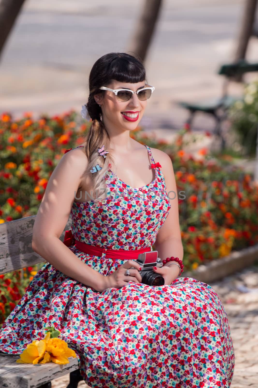 Pinup girl  with dress relaxing in the park, using a vintage camera.