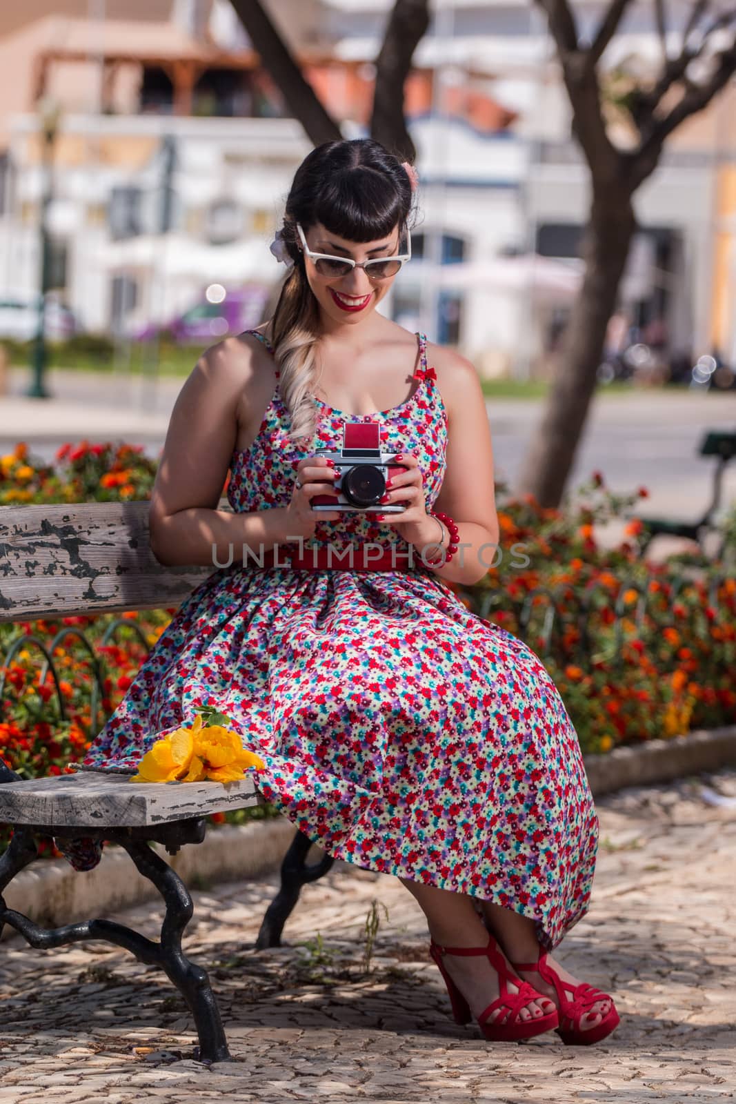 Pinup girl  with dress relaxing in the park, using a vintage camera.