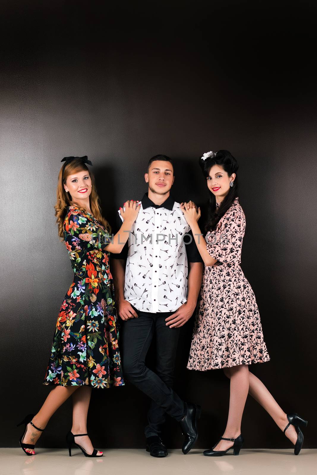 Two woman and a man posing on a vintage style retro clothing.