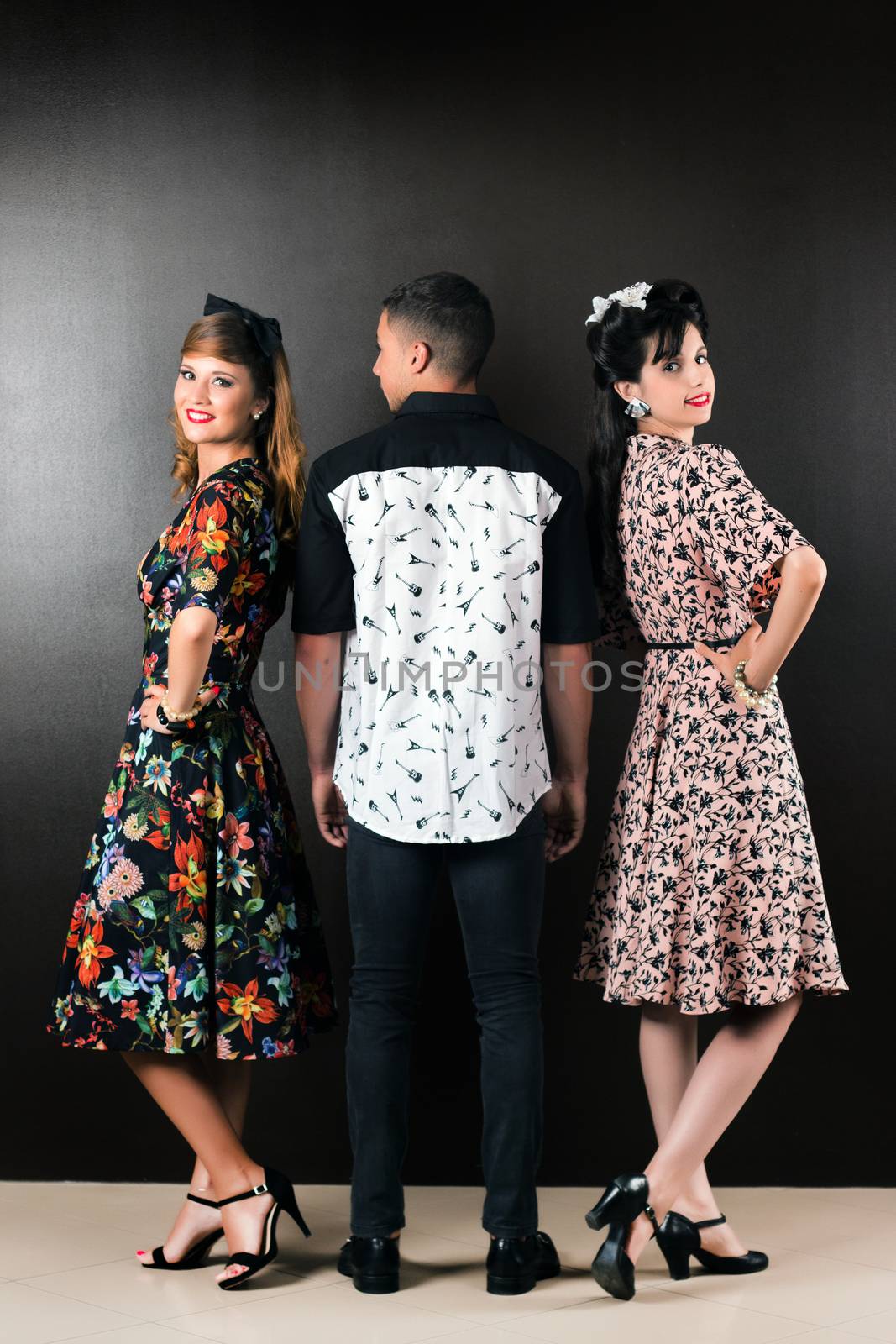 Two woman and a man posing on a vintage style retro clothing.