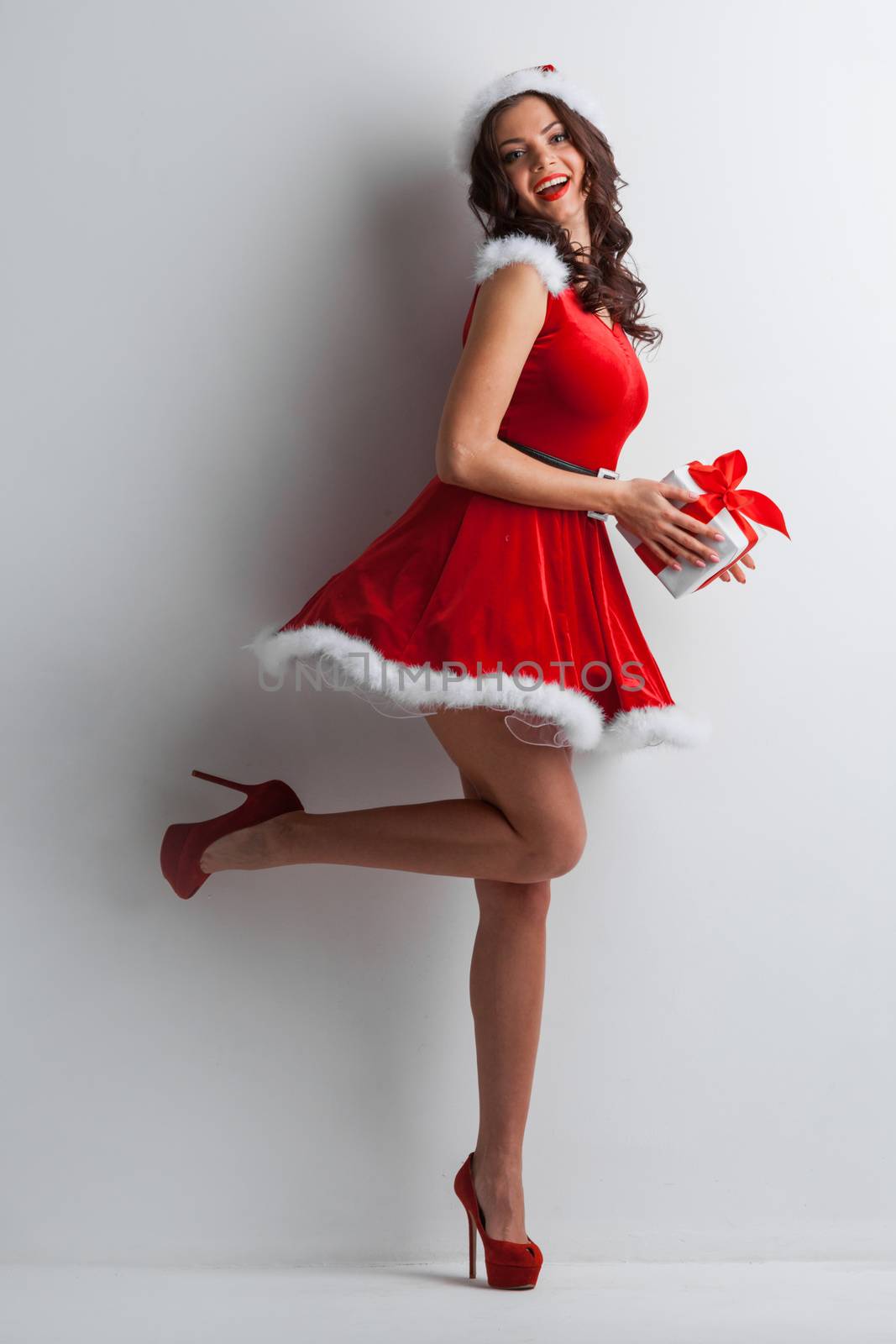Beautiful young woman in Santa hat celebrating Christmas holding gift box