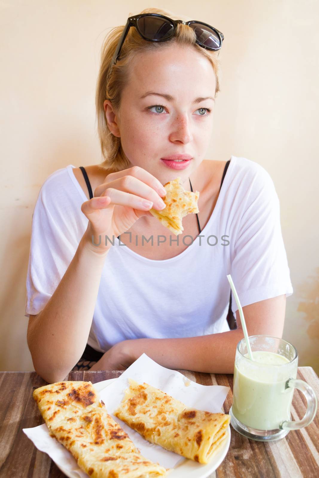 Female tourist eating delicious moroccan brakfast at one of street coffee shops: traditional pancakes with cheese and honey and avocado milkshake.