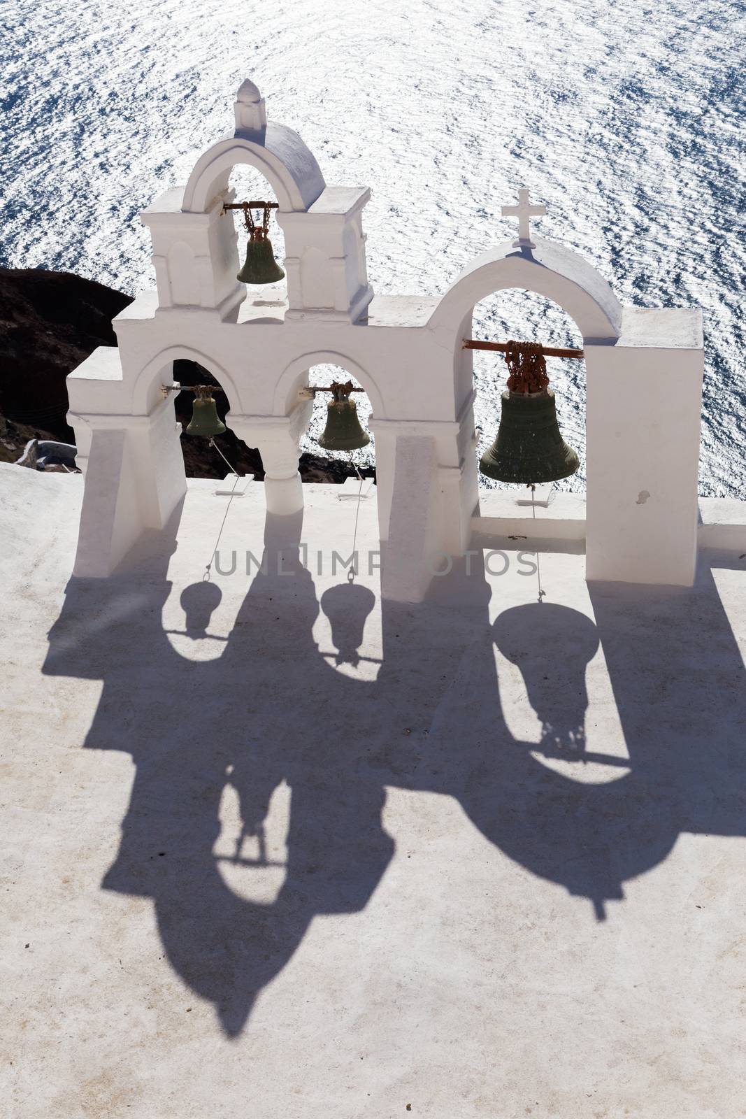 View of sea surface through traditional Greek white church arch with cross and bells in Oia village of Cyclades Island, Santorini, Greece.