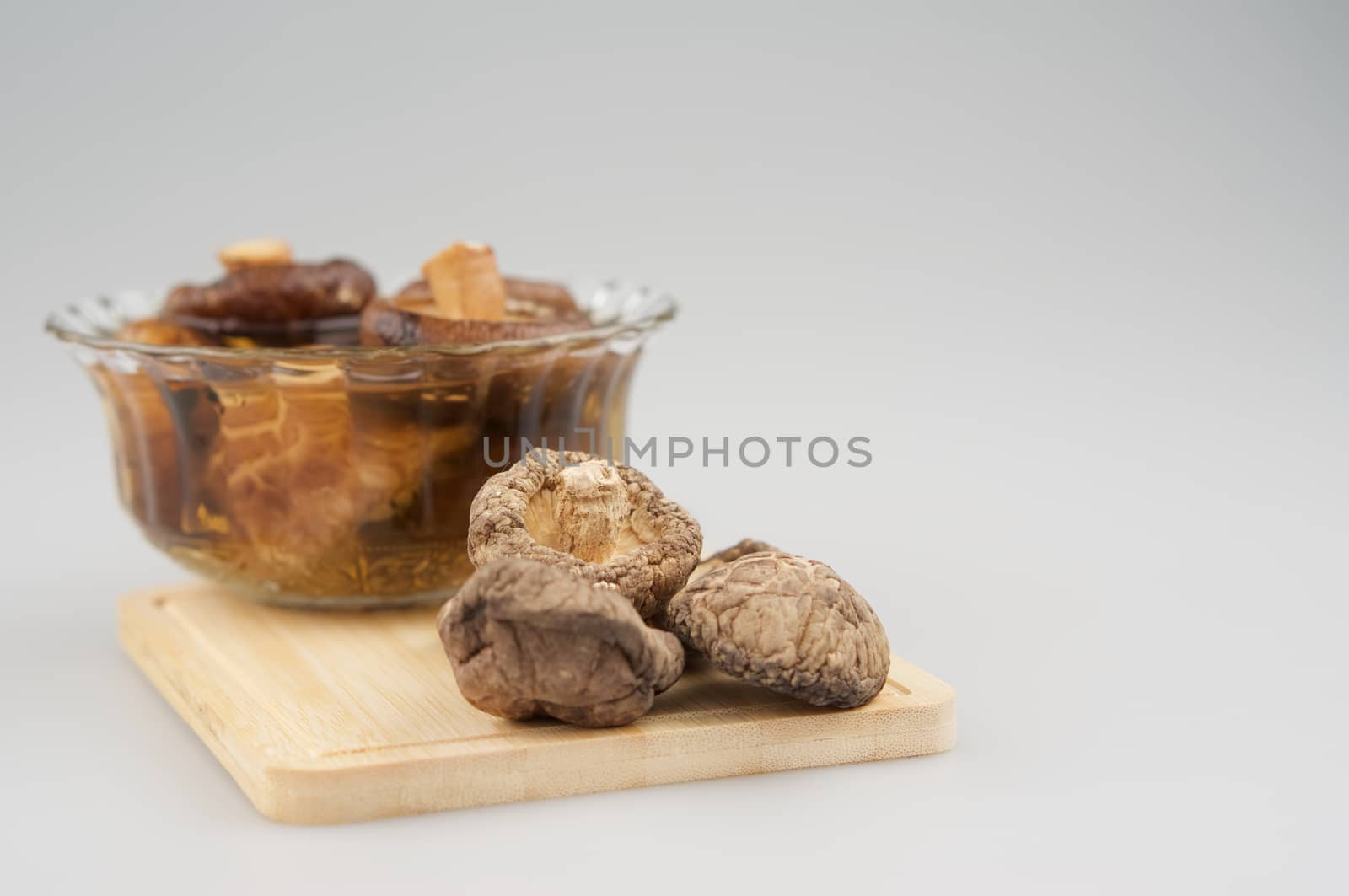 Dry Shitake mushroom or lentnus edodes place on chopping board have blur mushroom soak in glass cup as background photography with white background and copy space.