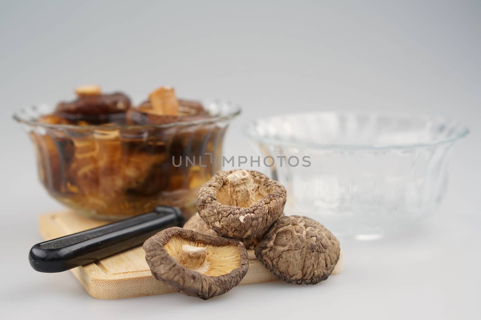 Dry Shitake mushroom or lentnus edodes and knife place on chopping board have blur mushroom soak and bowl as background photography with white background.