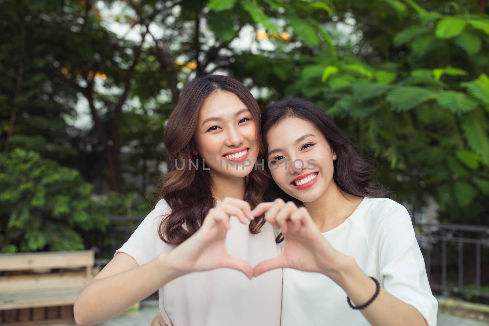 Woman couple having fun outdoors and making heart symbol