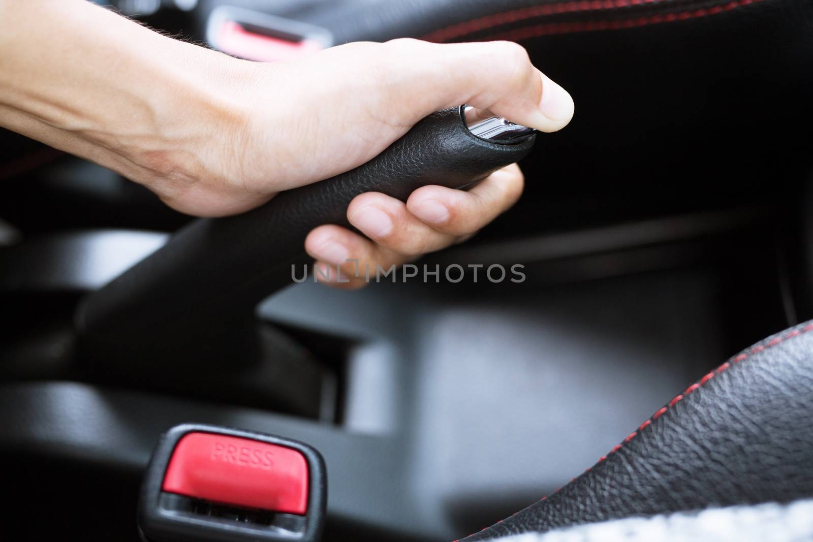 Closeup of young woman pulling handbrake lever in car For safety while parking.