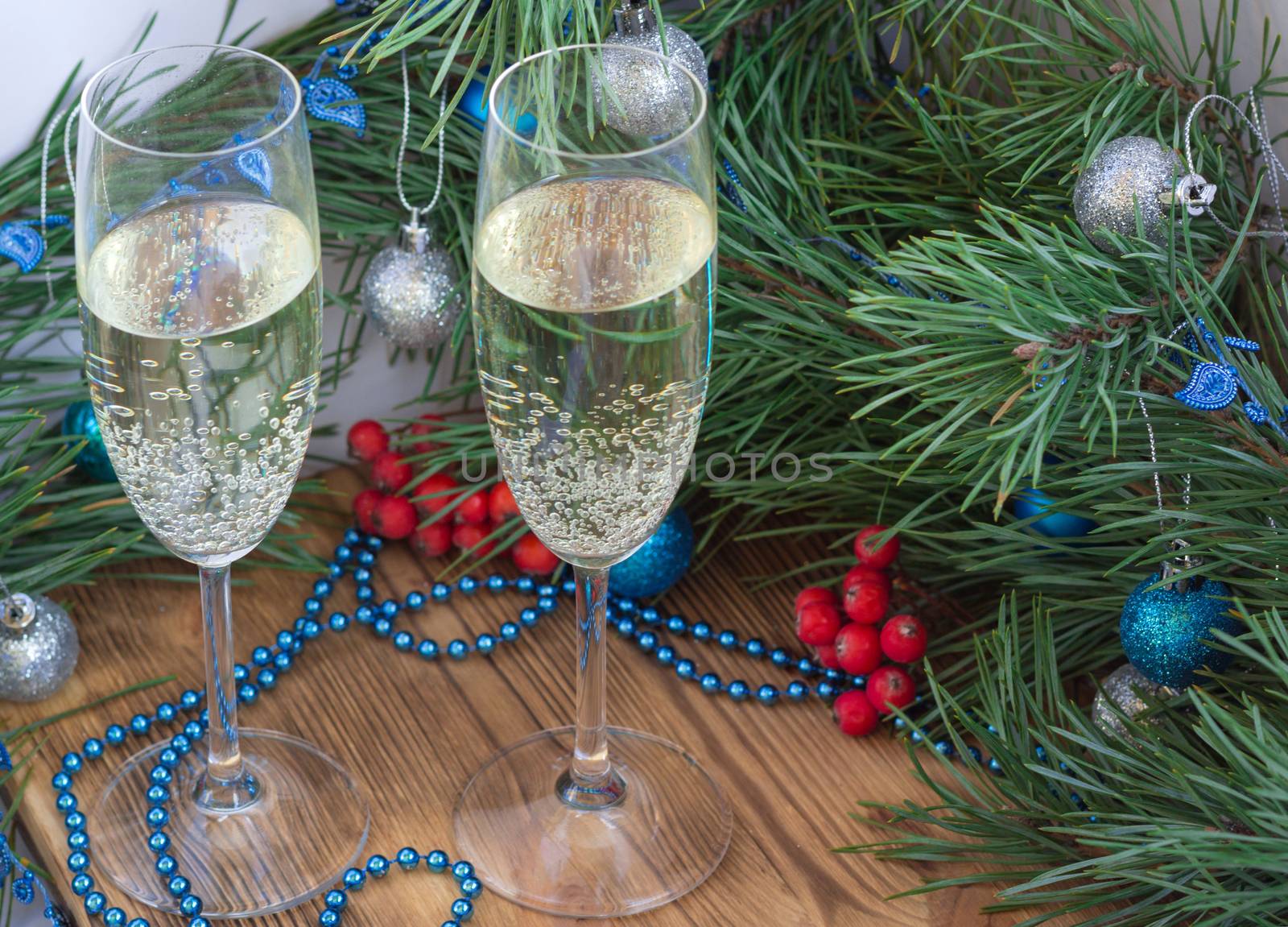 Christmas and New Year still life composition with two champaign glasses, pine tree acerose, red rowan berries, blue and silver balls, garland ornament decoration, copy space