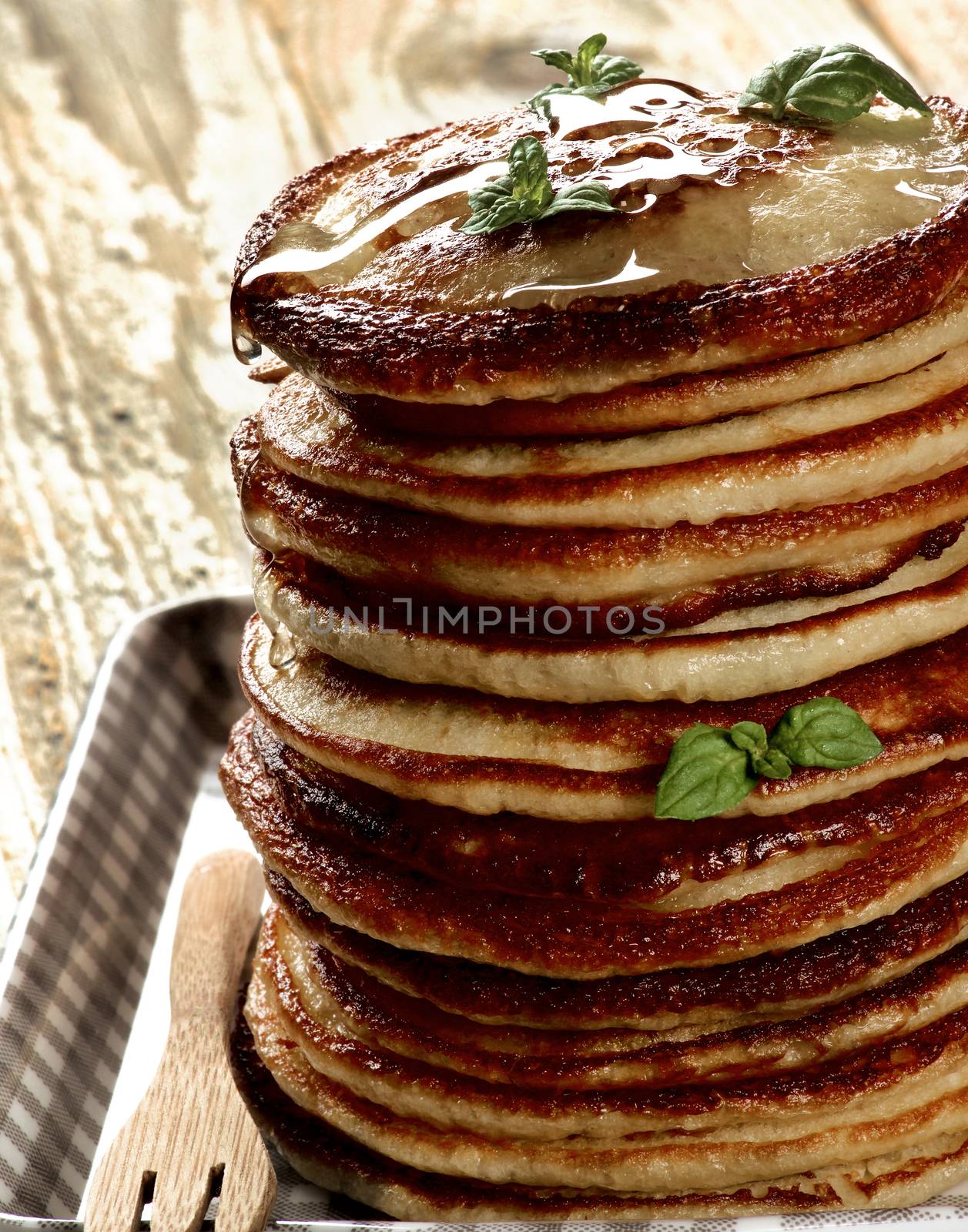Stack of Delicious Homemade  Pancakes with Honey  and Mint Leafs on Checkered Tray closeup on Wooden background