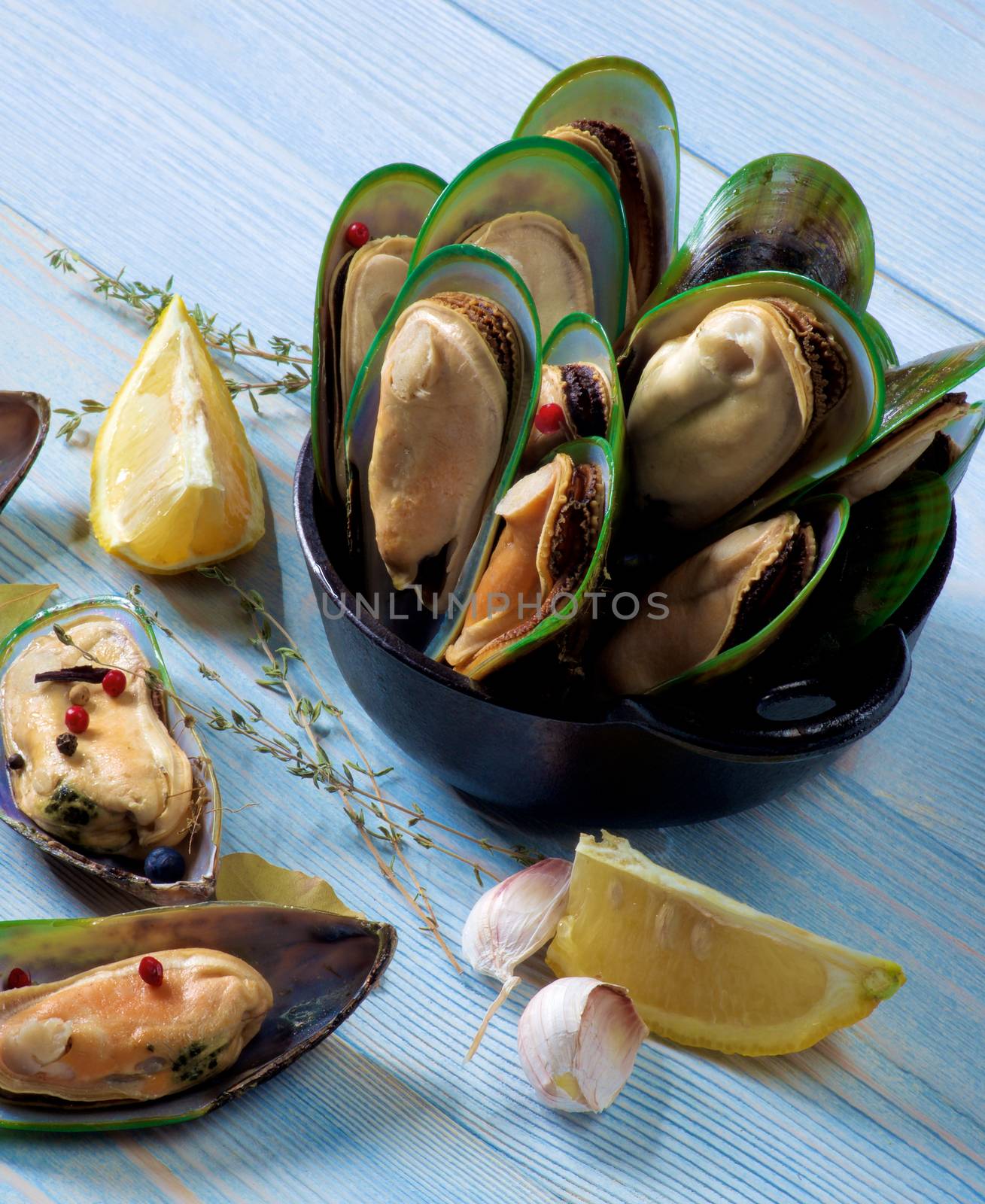 Arrangement of Fresh Boiled Green Mussels with Spices and Lemon in Black Iron Cast closeup on Blue Wooden background