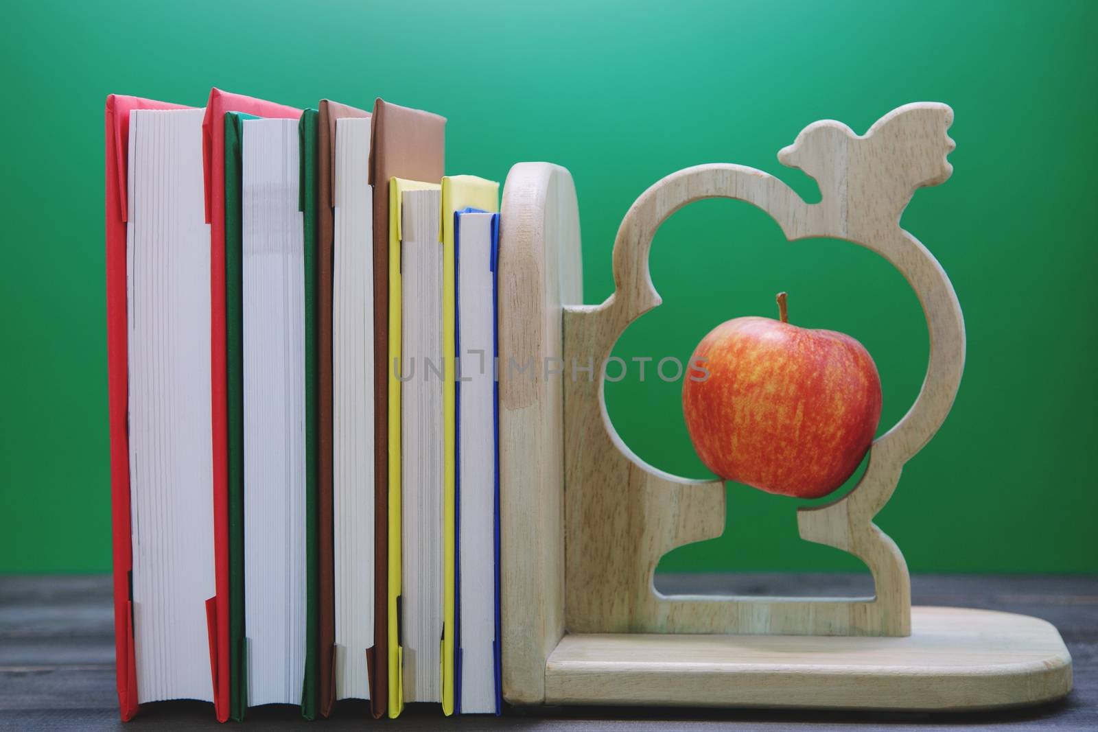 School books many on desk. and Equipment along with bookmark and apple.