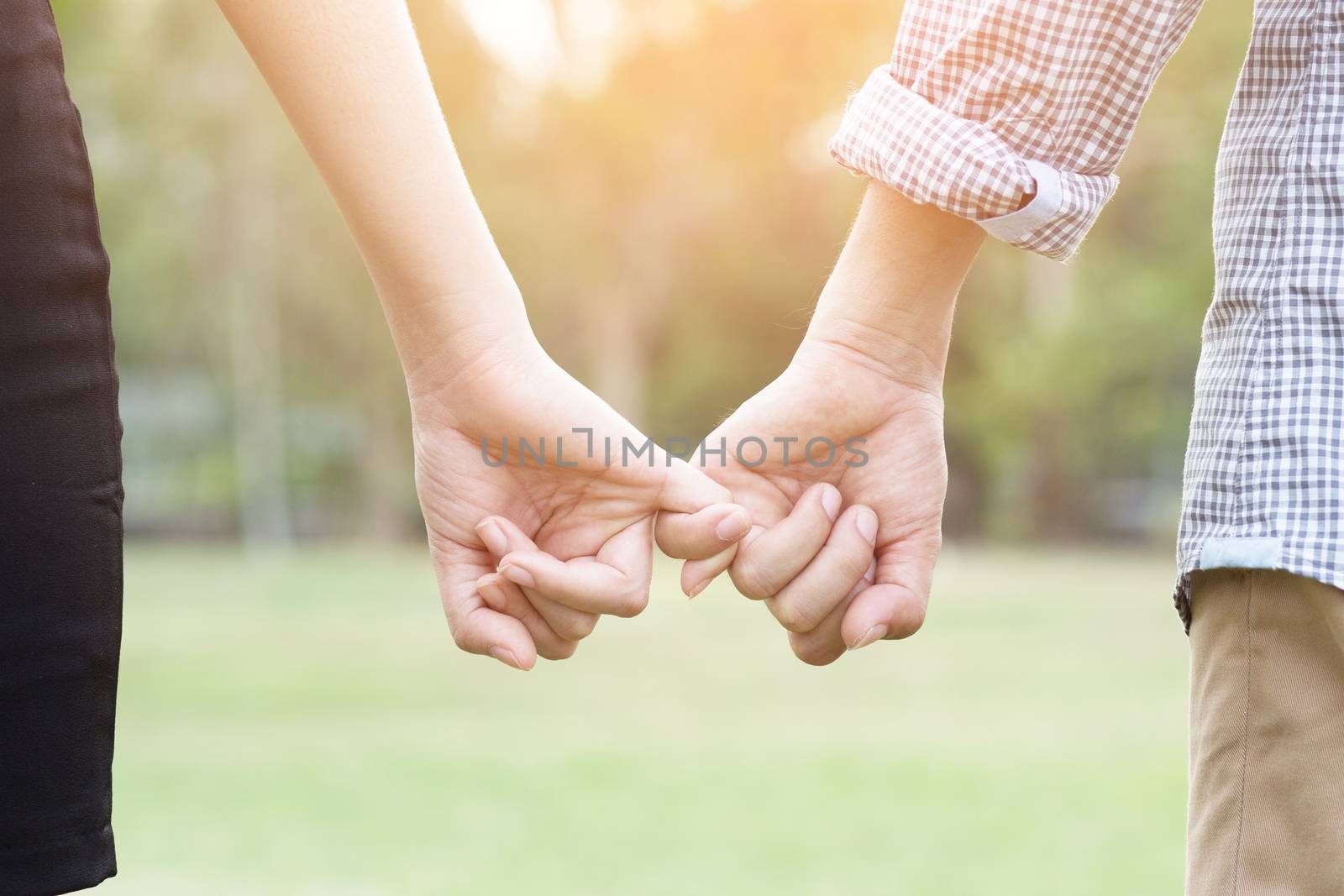 Couple lovers holding hands towards the sun with bright sun flare in parks, or close up view in a conceptual image first love and puppy love adolescent young.