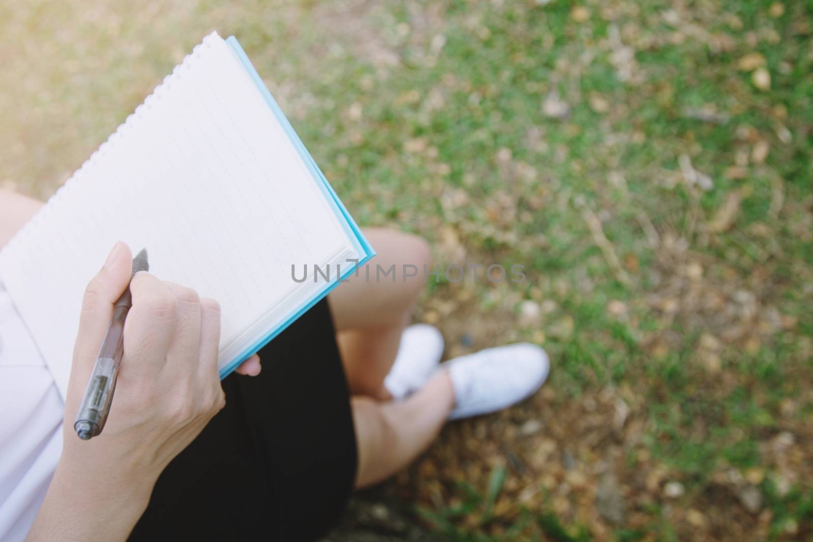 Woman's hand take notes with a pen on a notebook in garden.