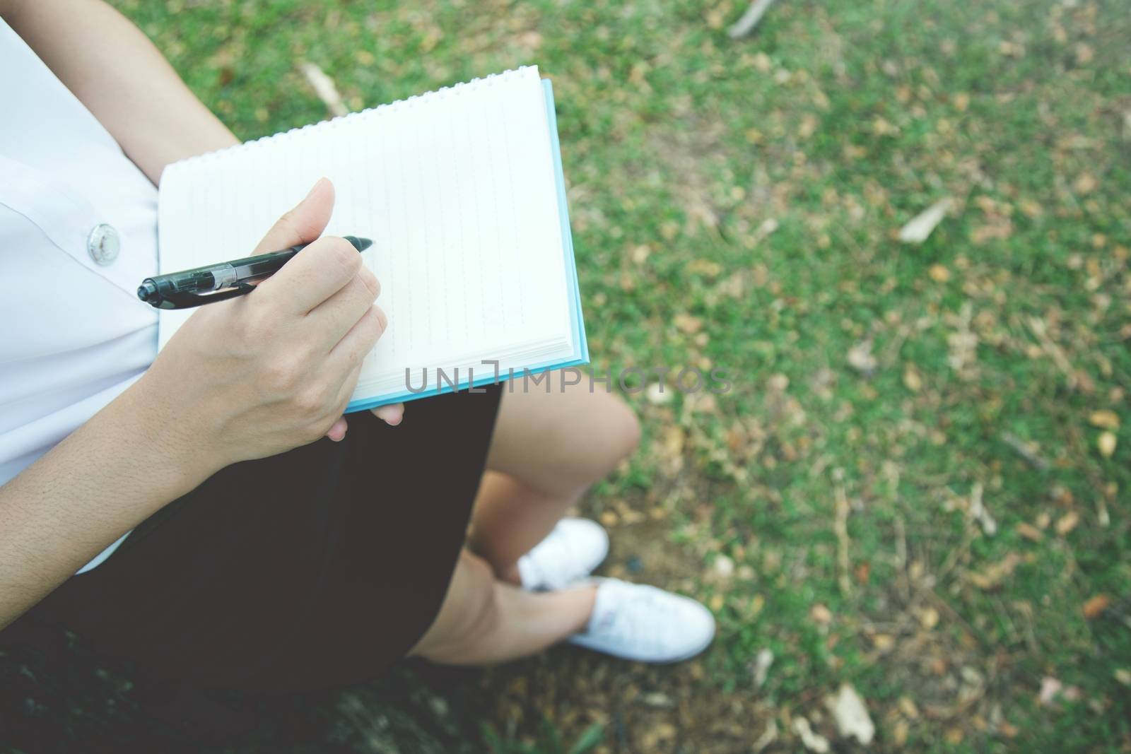 Woman's hand take notes with a pen on a notebook in garden.