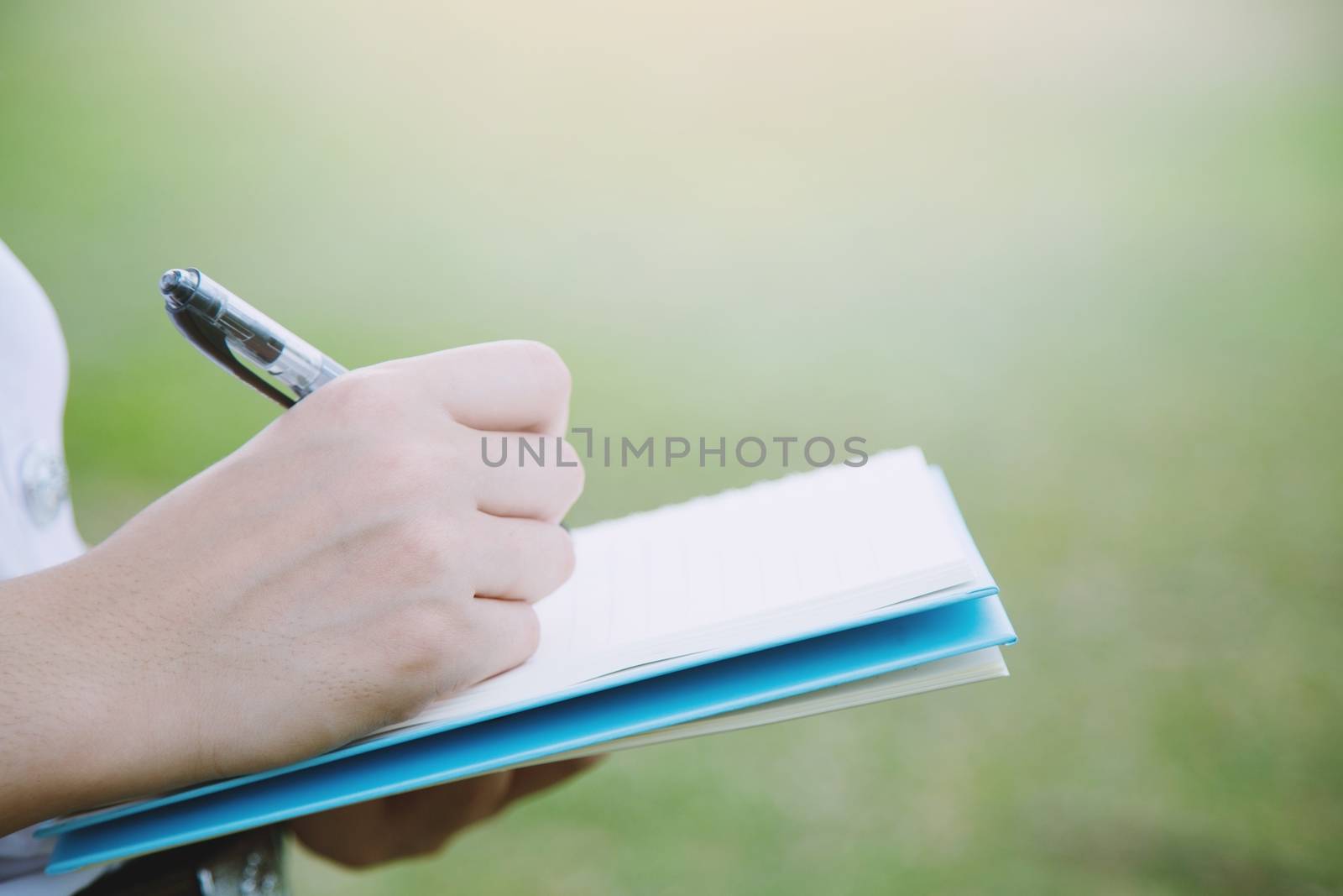 Woman's hand take notes with a pen on a notebook in garden.