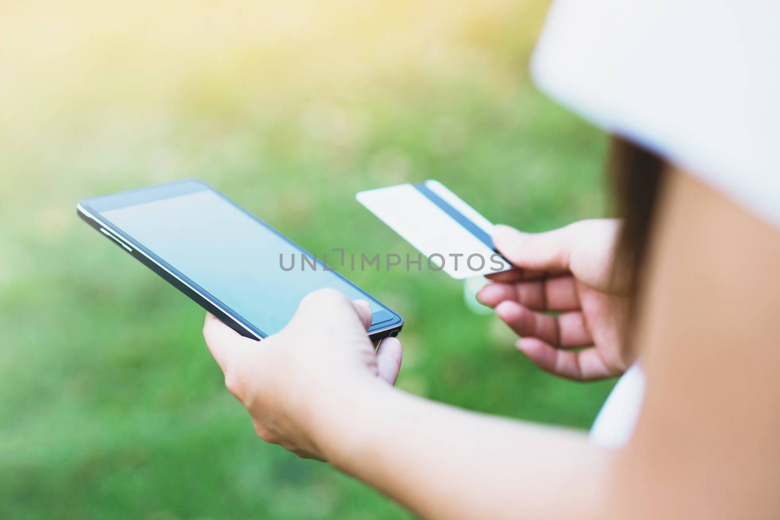 hands holding a credit card and using cell phone online shopping outdoor. by boytaro1428@gmail.com