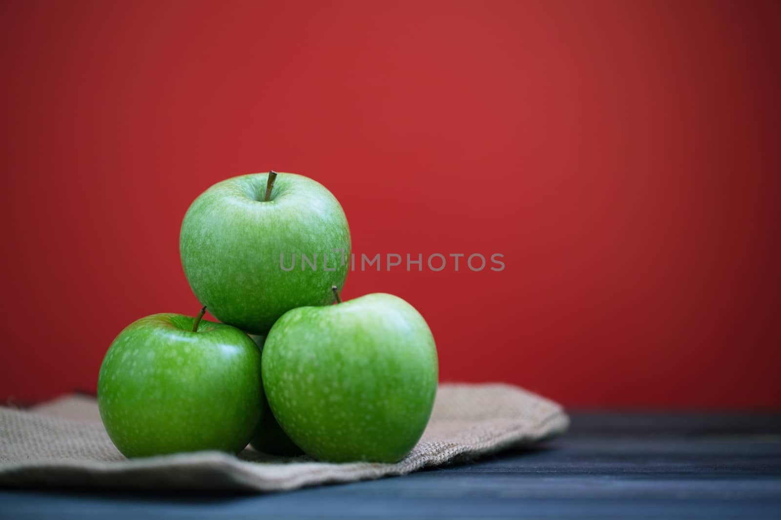 Group of green apples with fresh on a sack in a wooden desk and Red background.